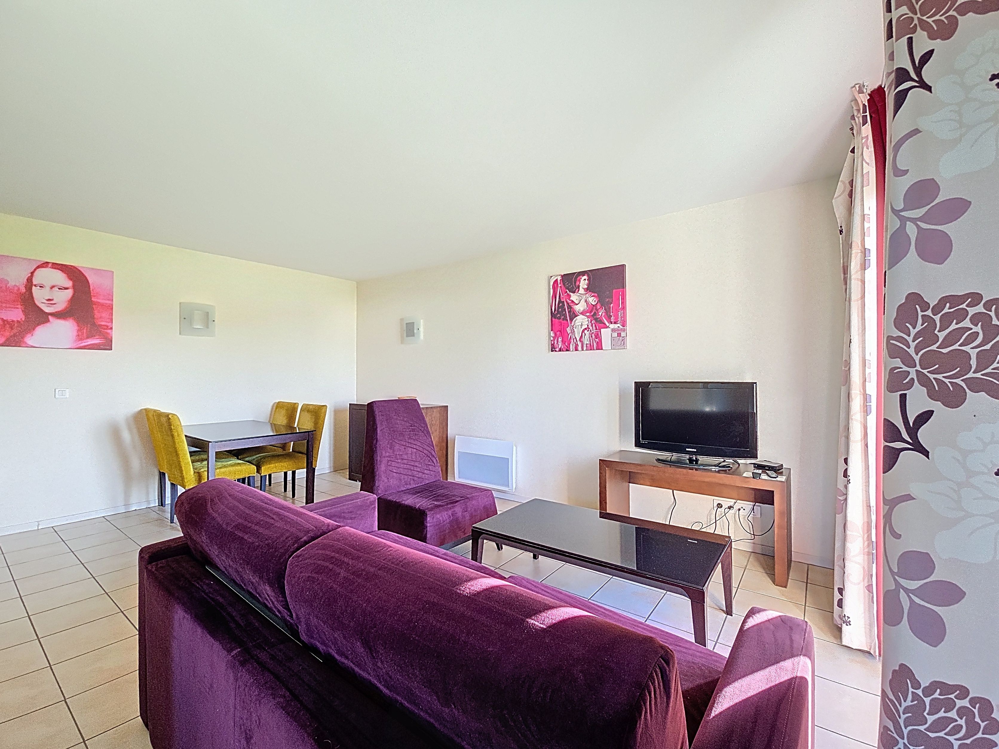 image Living area with purple sofa, black coffee table, and yellow dining chairs — sofa converts to a double bed