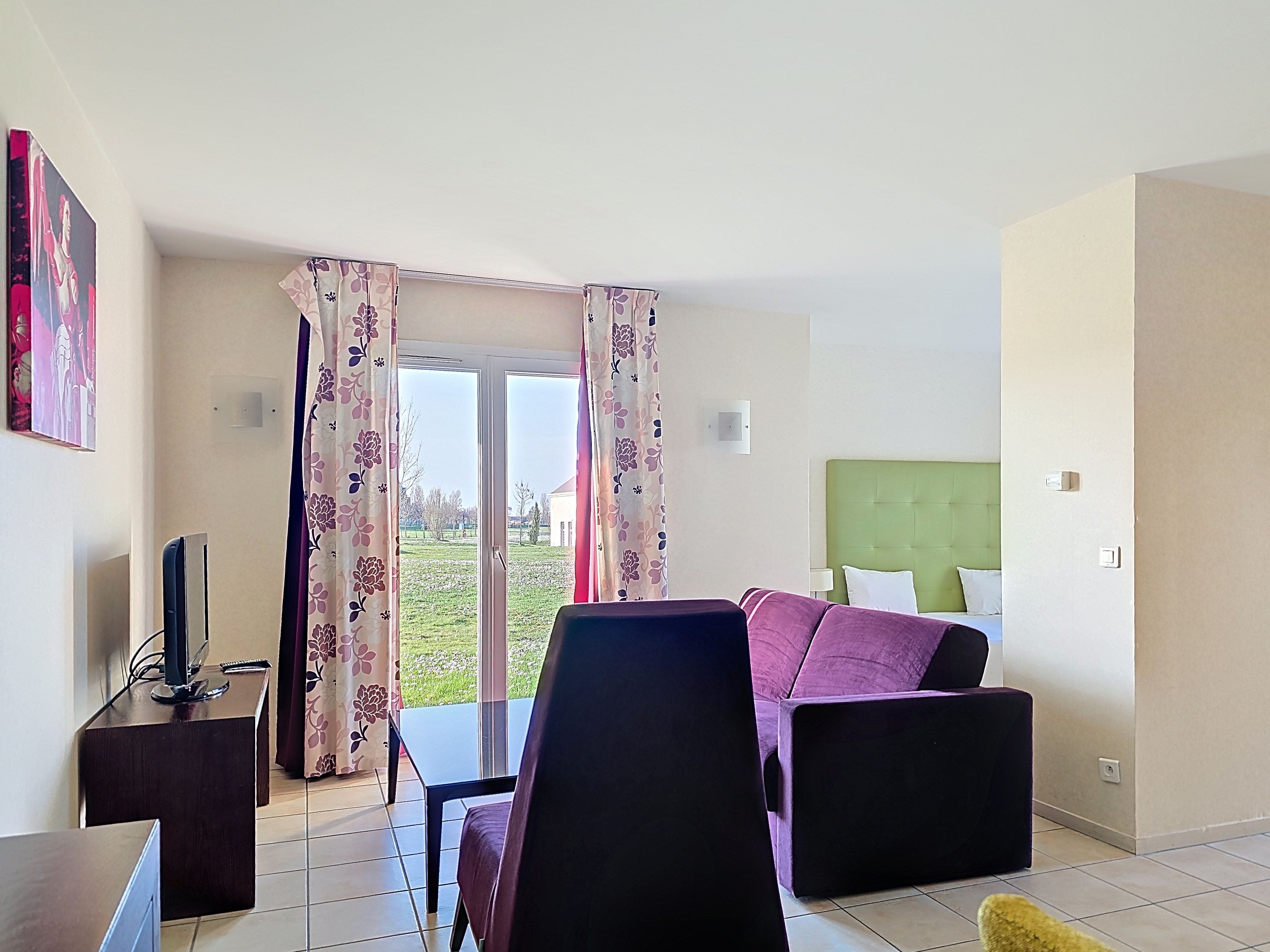image Patio doors in the living area open to outdoor space, with a green-headboard bed visible in the background