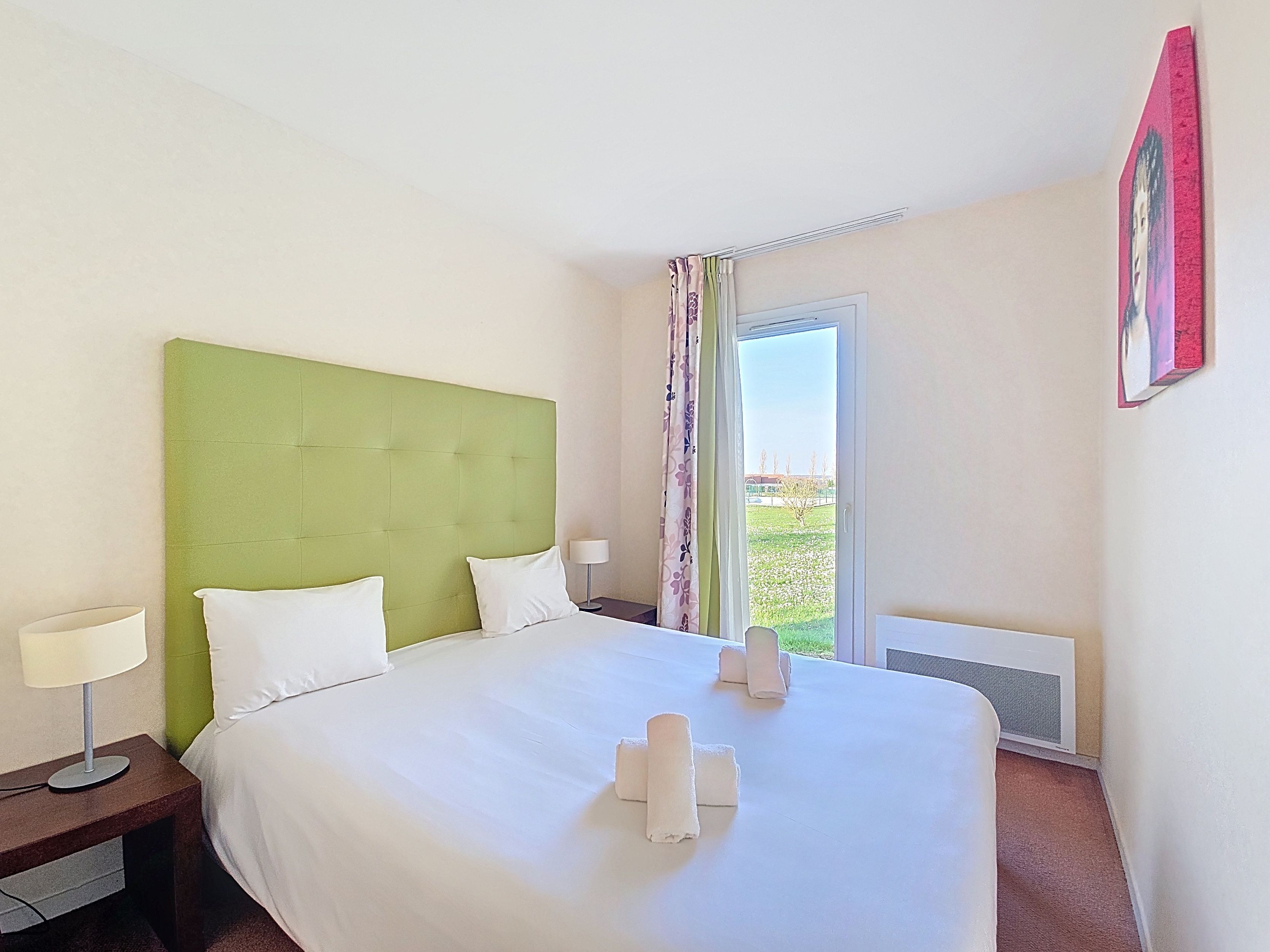 image Bedroom with green padded headboard, white linens, bedside tables with lamps, and a window onto the grounds