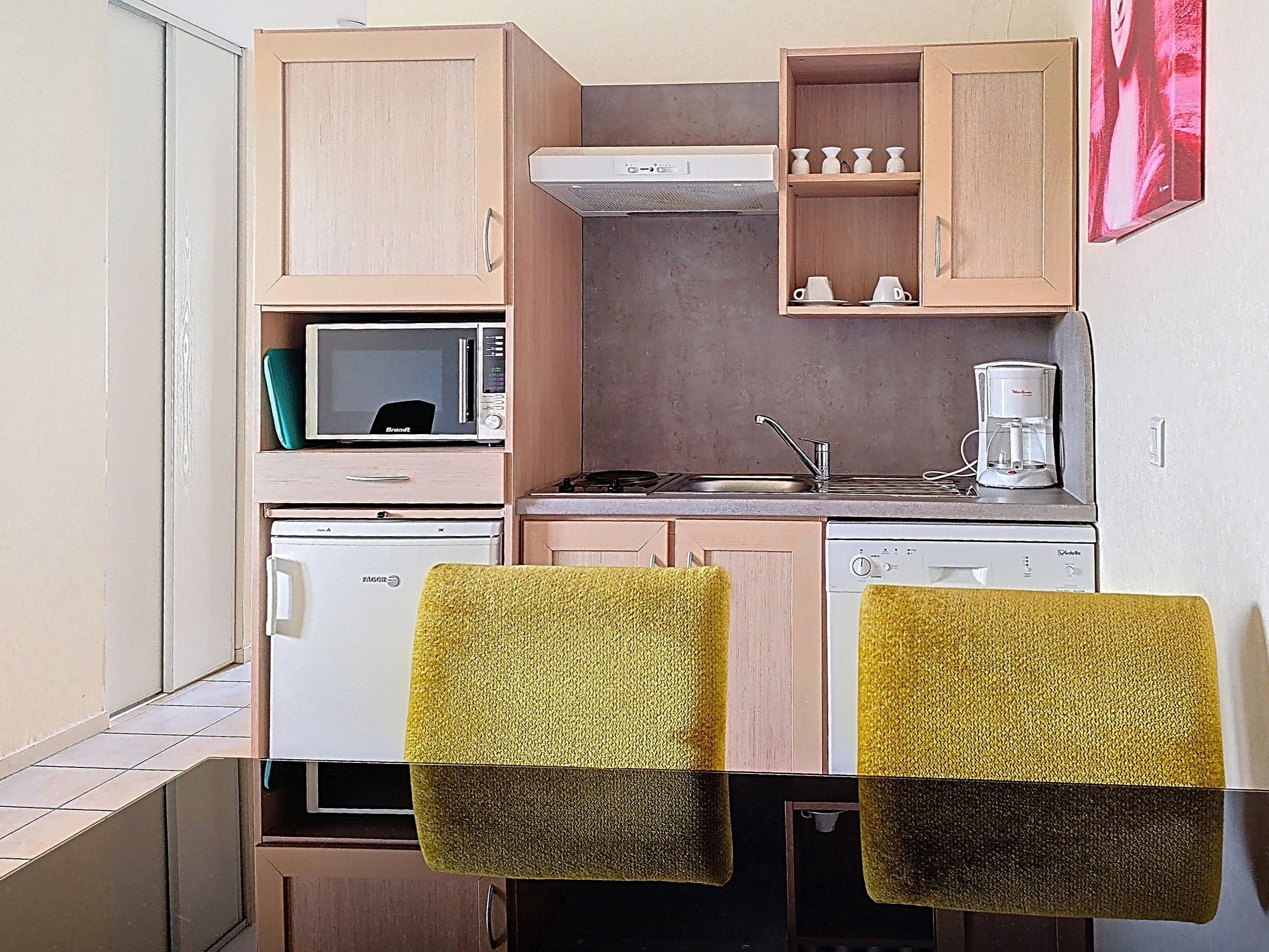 image Kitchen corner with light wood cabinets, microwave, dishwasher, and fridge — green dinnerware on the shelf