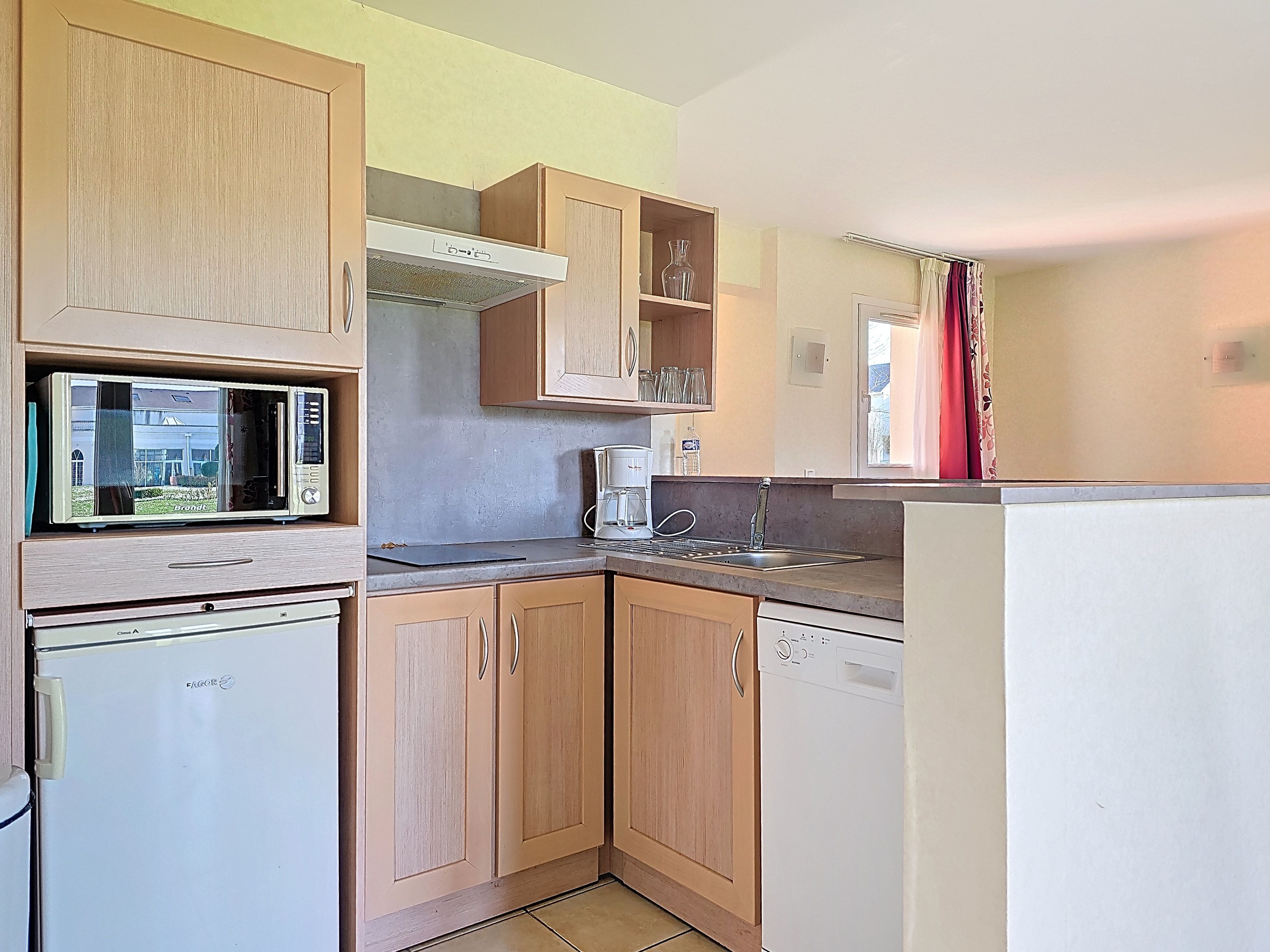 image Kitchen with light wood cabinets, white microwave and dishwasher, grey countertop, and space for a full group