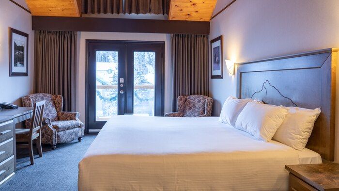 image King bed under a vaulted pine ceiling with balcony doors leading to mountain views