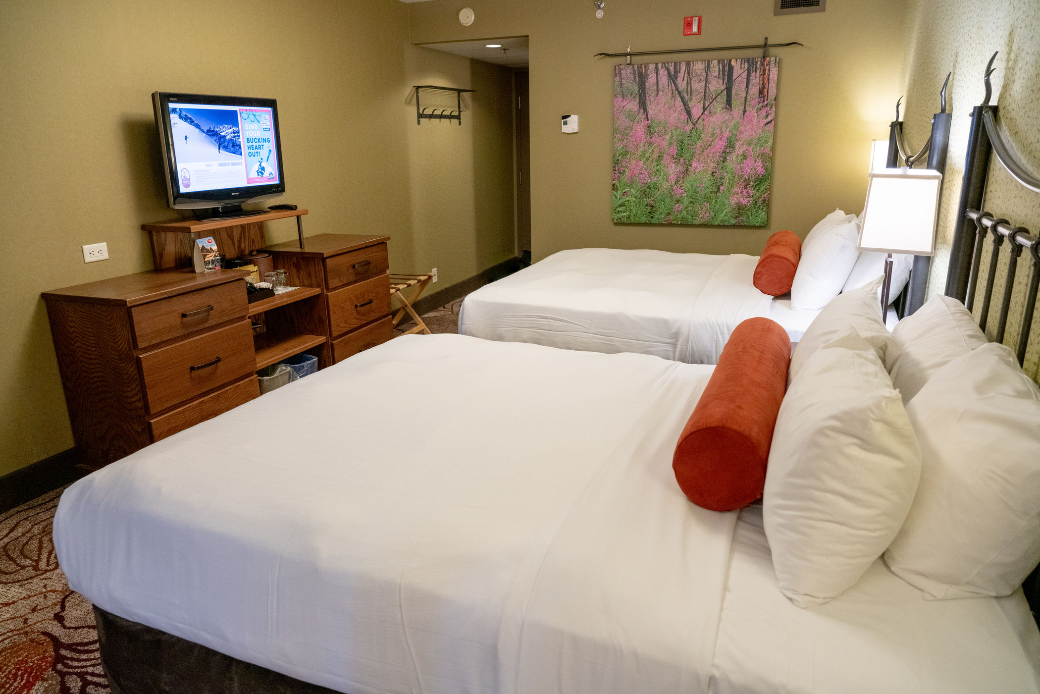 image Two queen beds with Mountain Luxury bedding face the flatscreen TV — room for the whole family after a day on the trails.