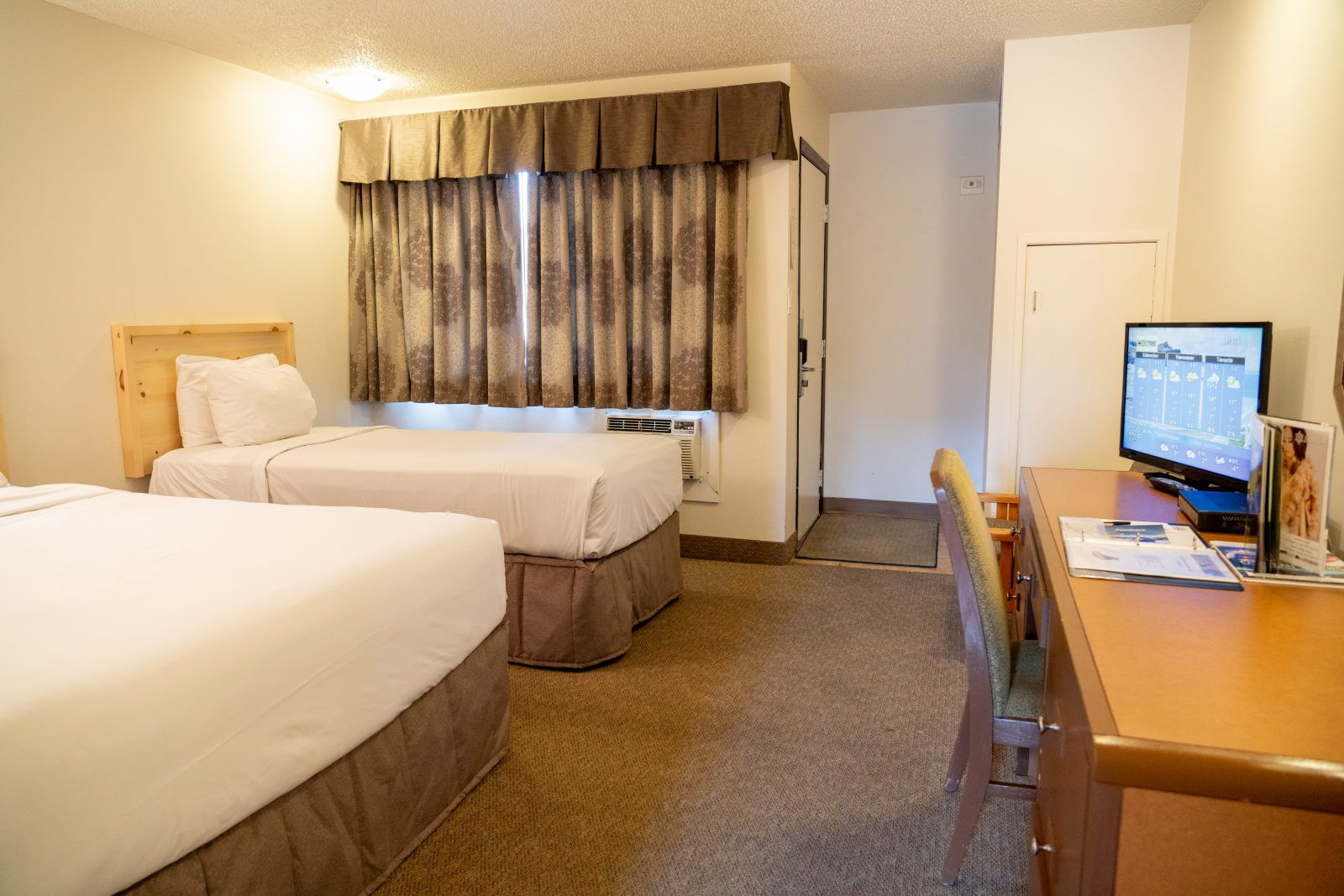 image Wide-angle view of the sleeping area with two beds, desk, and TV — plus a doorway to the kitchen