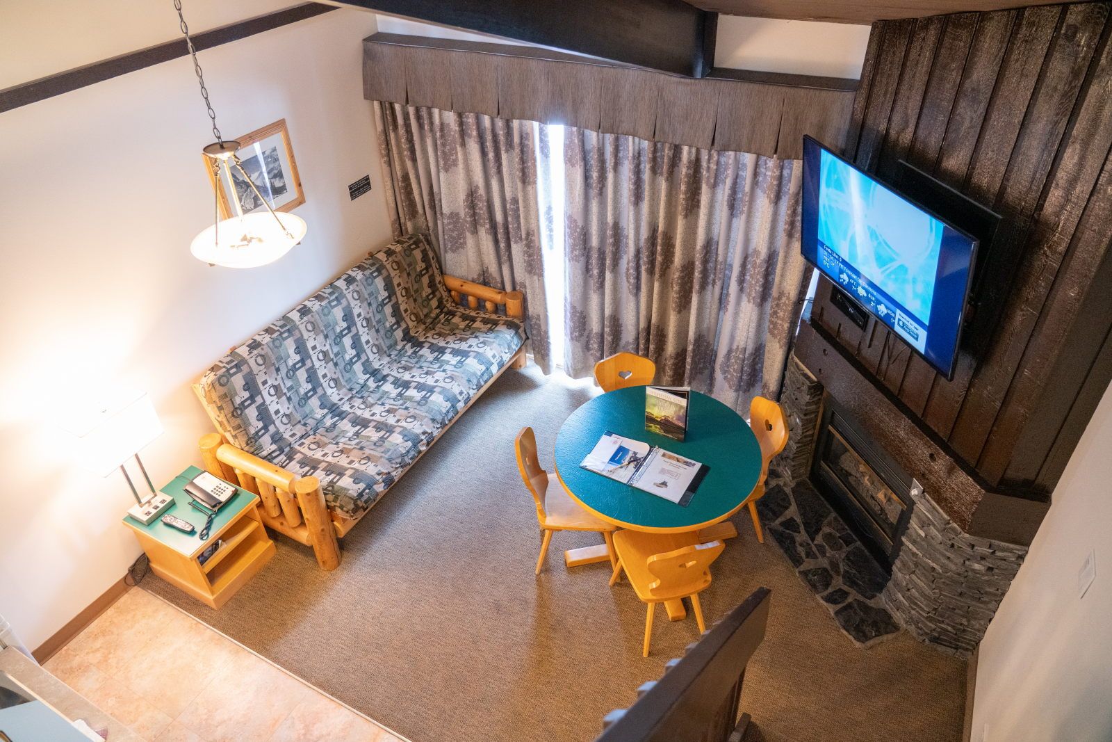 image Overhead view of the living area — teal dining table, log sofa, fireplace, and staircase up to the loft