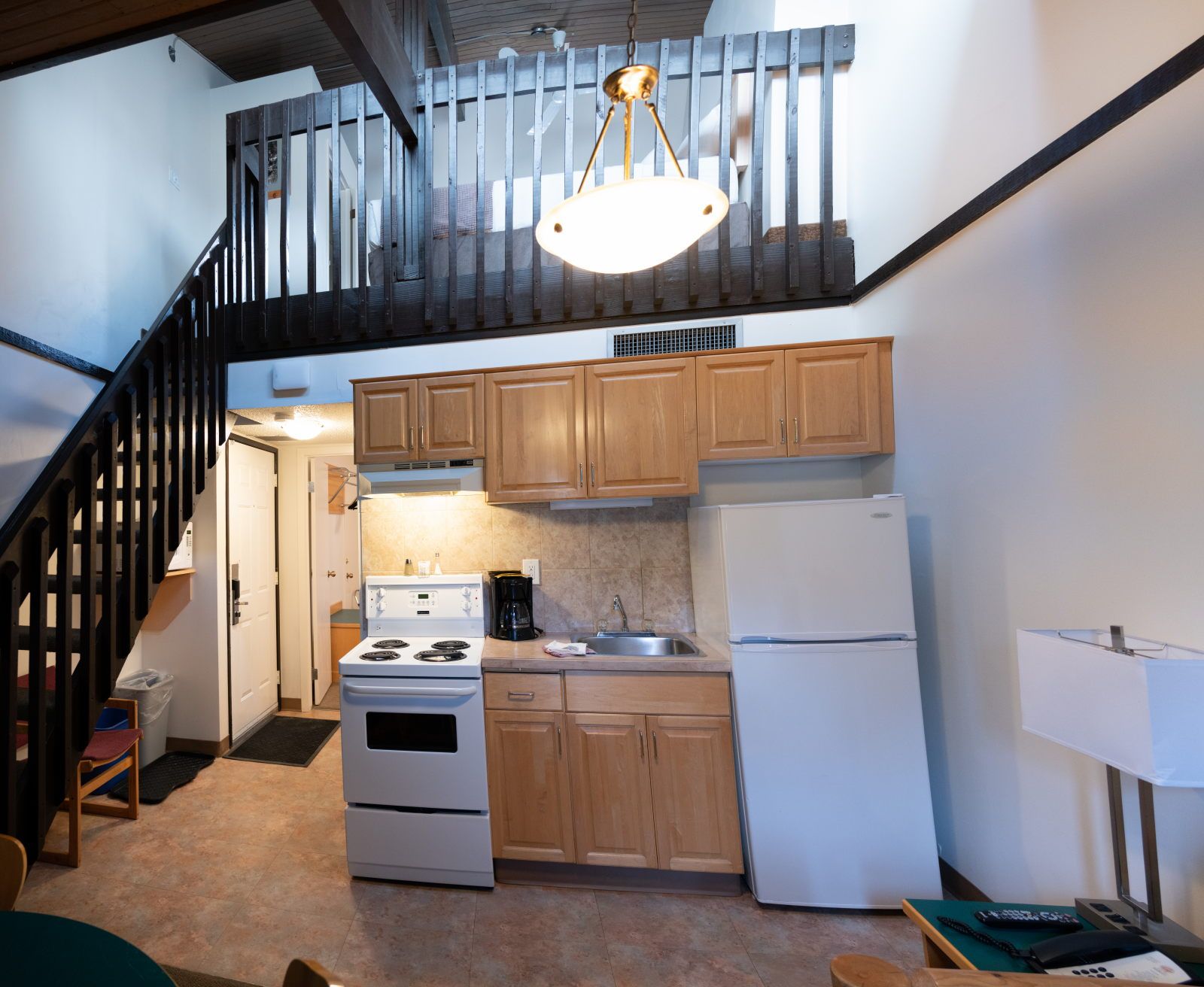 image Open kitchen with light wood cabinets, white stove, fridge, and coffee maker — stairs to loft just behind