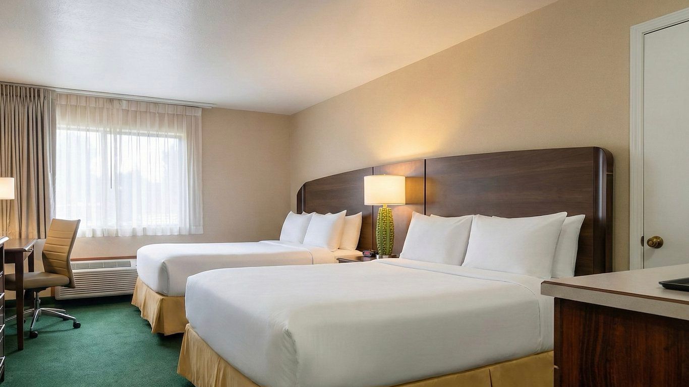 image Bright room with two queen beds and a work desk near the window.
