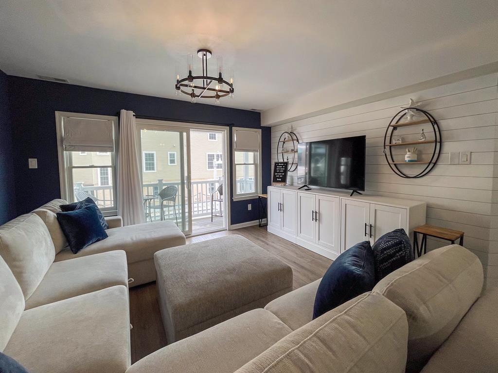 image Open-plan living room with a large sectional sofa, wall-mounted TV, and sliding doors out to the balcony.