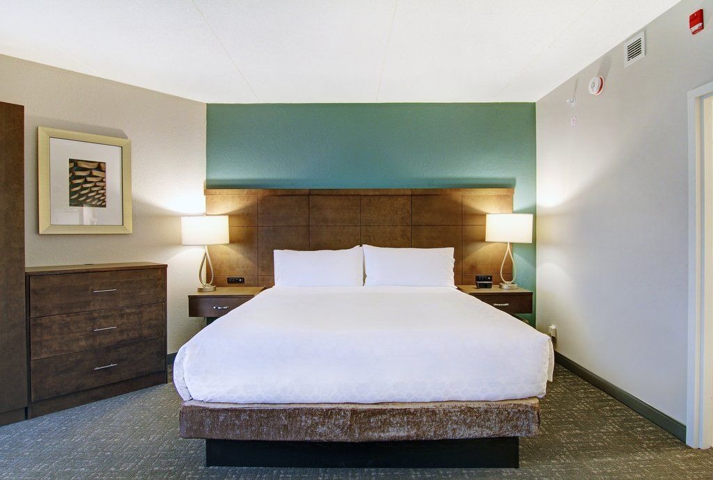 image Warm-toned king bed with crisp white linens in the open-plan sleeping area — accessible layout with clear floor space throughout.