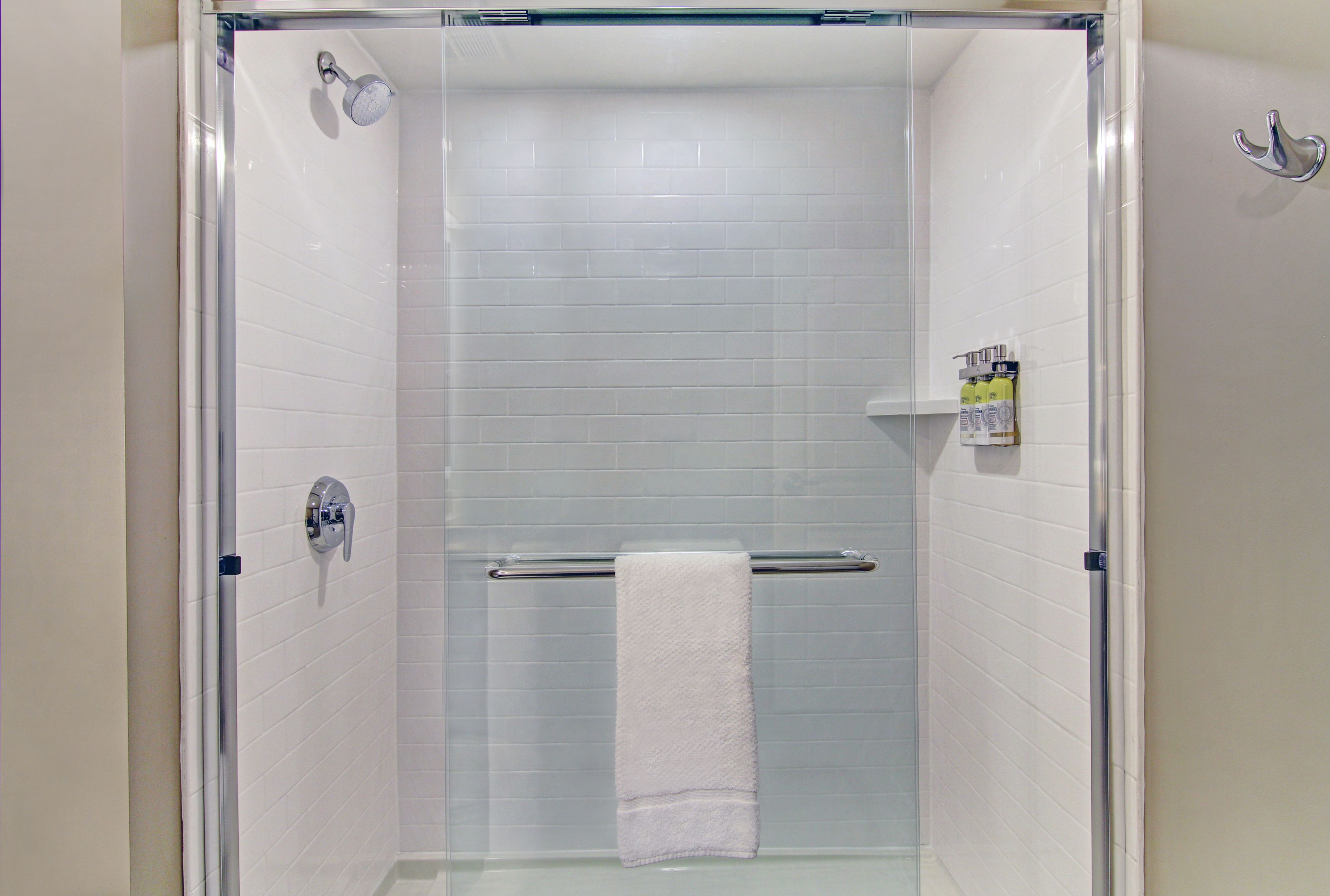 image Glass-enclosed shower with white subway tiles, chrome towel bar, and built-in toiletry shelf — towels and toiletries provided.