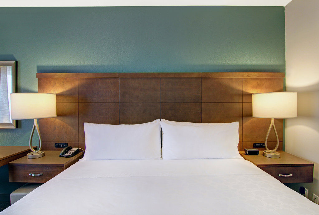 image King bed with white linens and a wooden headboard — open-plan studio layout with work desk and flat-screen TV in the same space.
