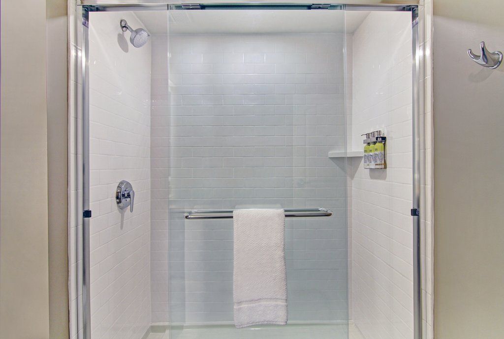 image Glass shower stall with white subway tiles, chrome fittings, and wall-mounted toiletry dispensers — towels provided.