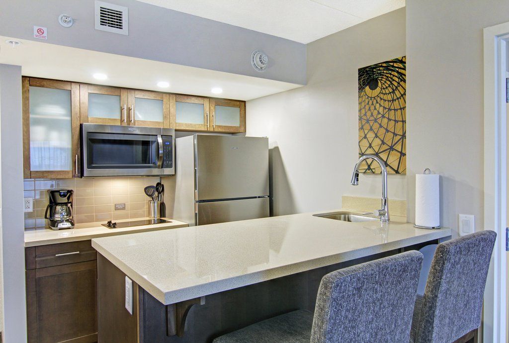 image Dark wood kitchen cabinets with stainless steel fridge, stovetop, and overhead microwave — bar stools at the island for casual in-suite dining.