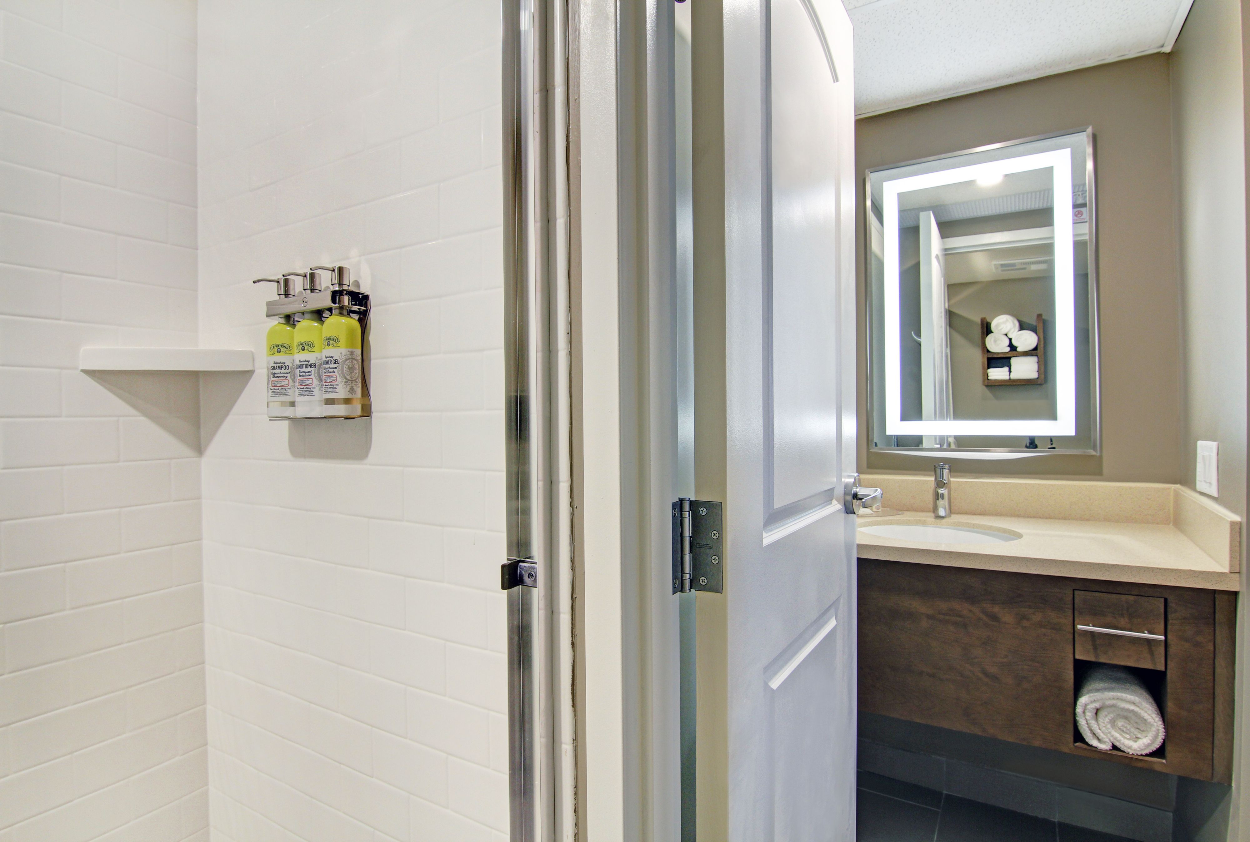 image Shower with white tile walls, glass door, and wall-mounted toiletry dispensers — towels provided.