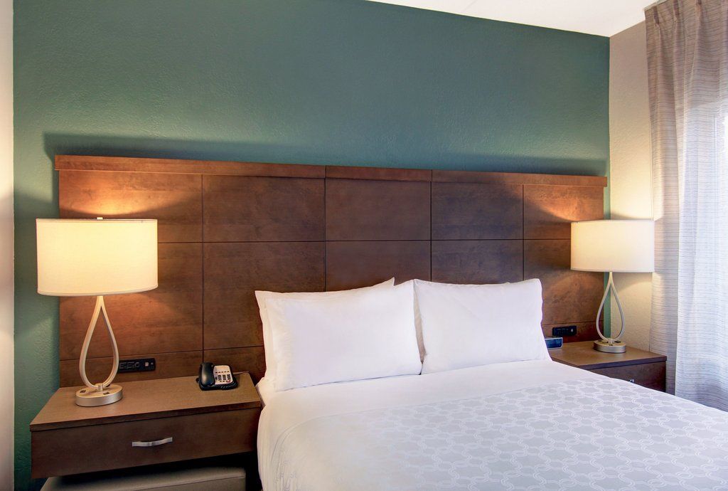 image Queen bed with white linens and a wooden headboard against a teal accent wall — one of two private bedrooms in the suite.