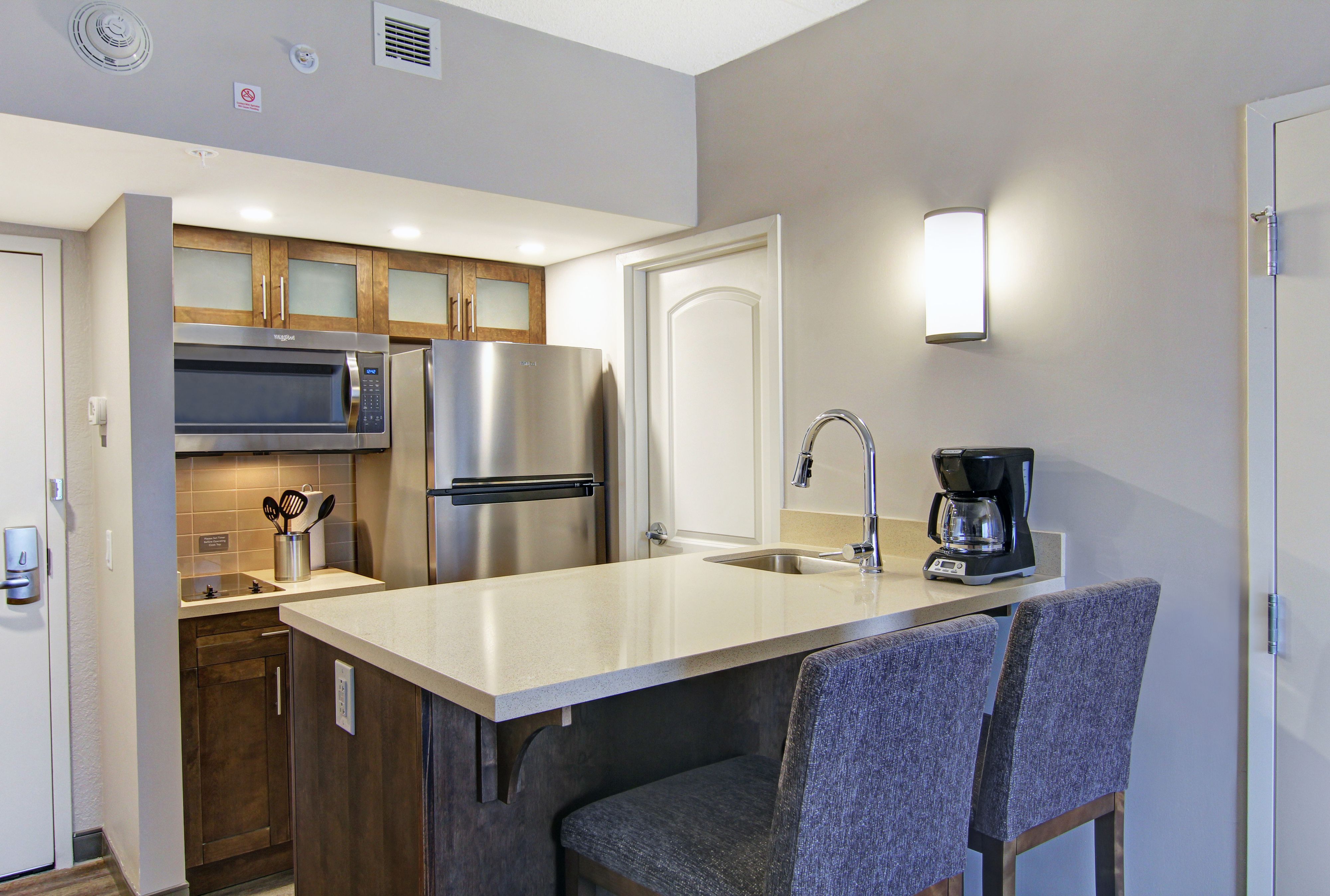 image Fully equipped kitchen with stainless steel fridge, overhead microwave, glass-front cabinets, and bar seating for two.