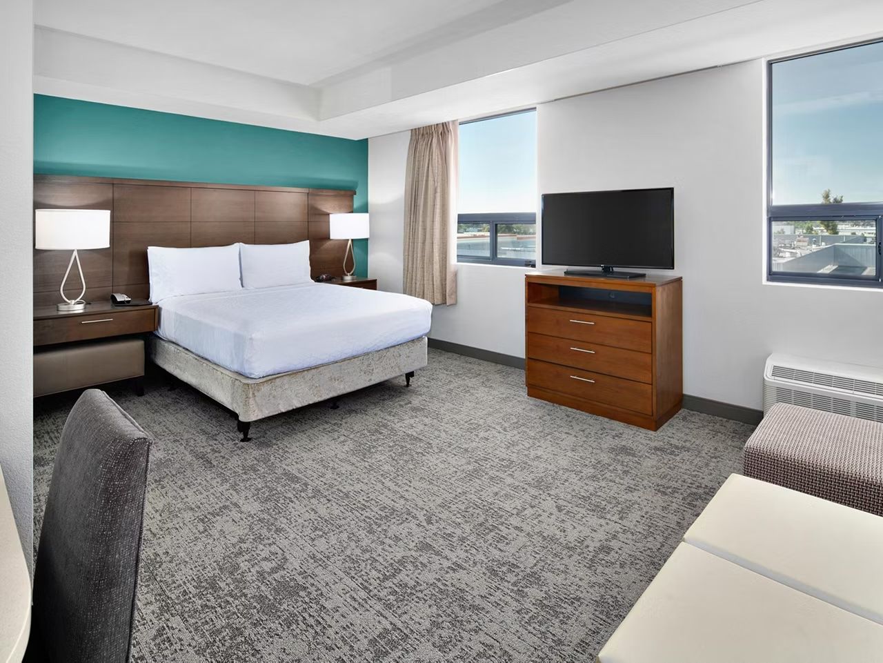 image Queen bed with teal accent wall, bedside lamp, and workspace — your private retreat after a day out.