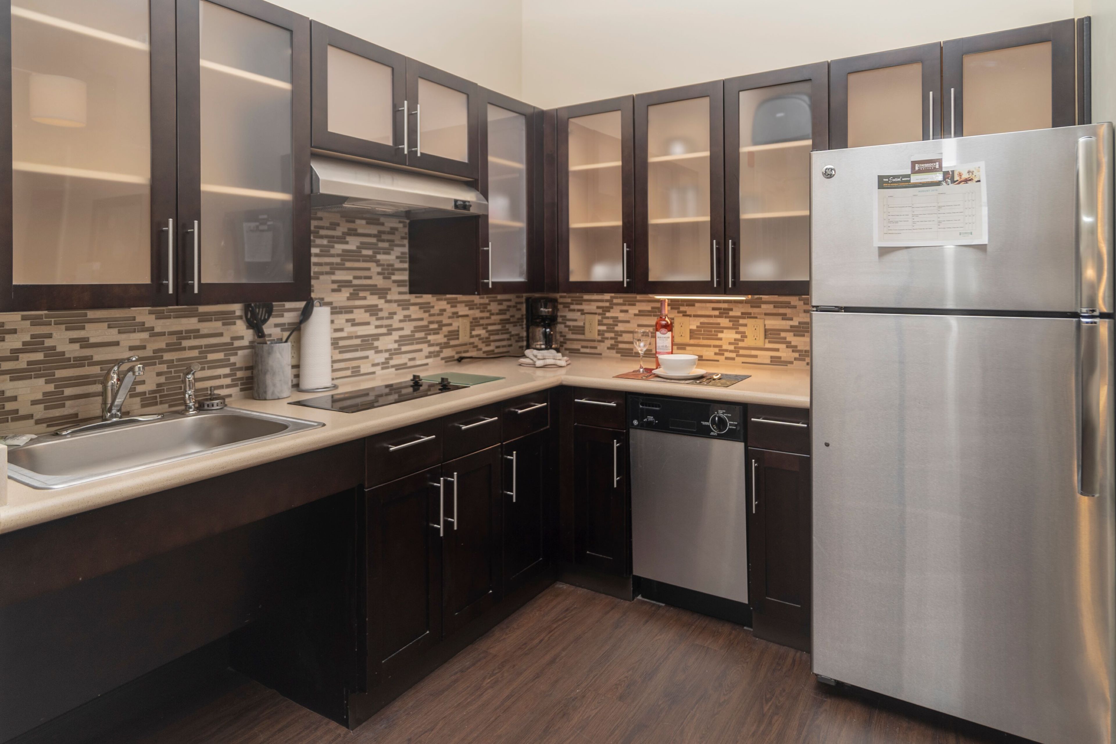 image Fully equipped kitchen with dark cabinetry, mosaic tile backsplash, and stainless steel appliances.