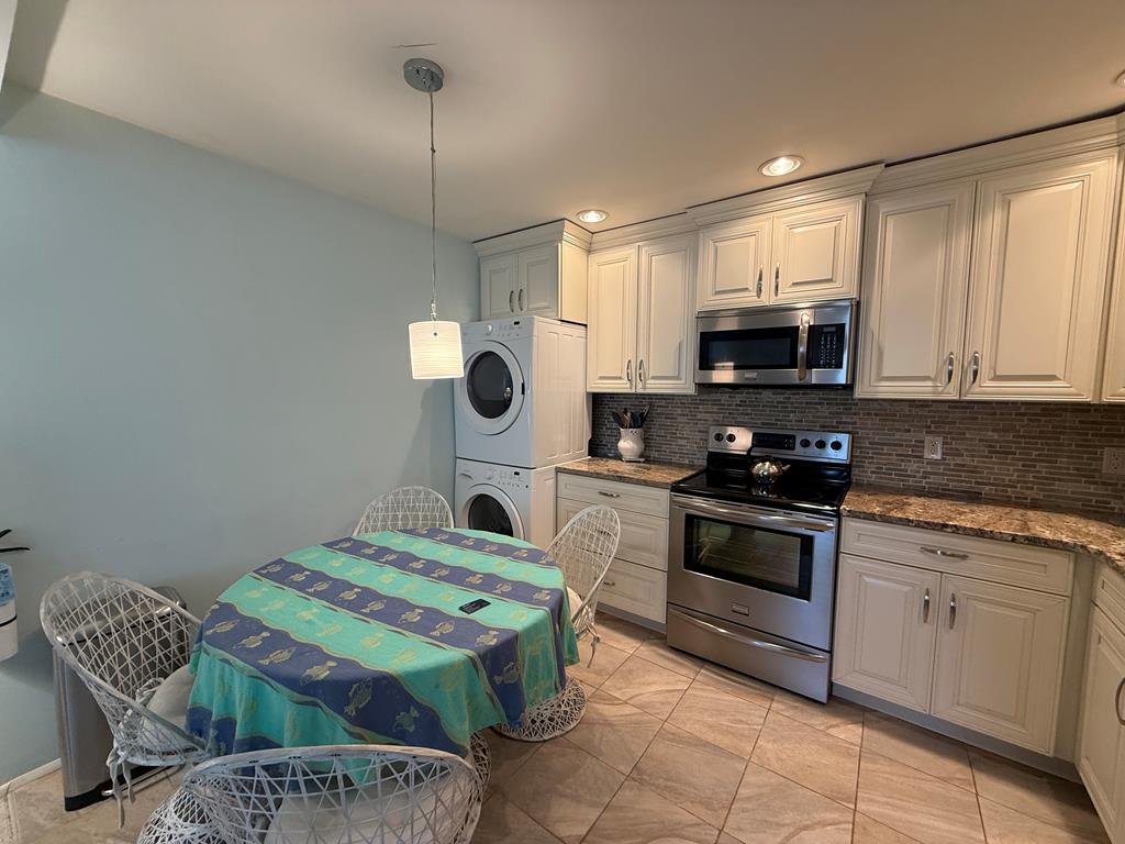 image Bright kitchen with granite counters, white cabinets, dining table, and laundry appliances.