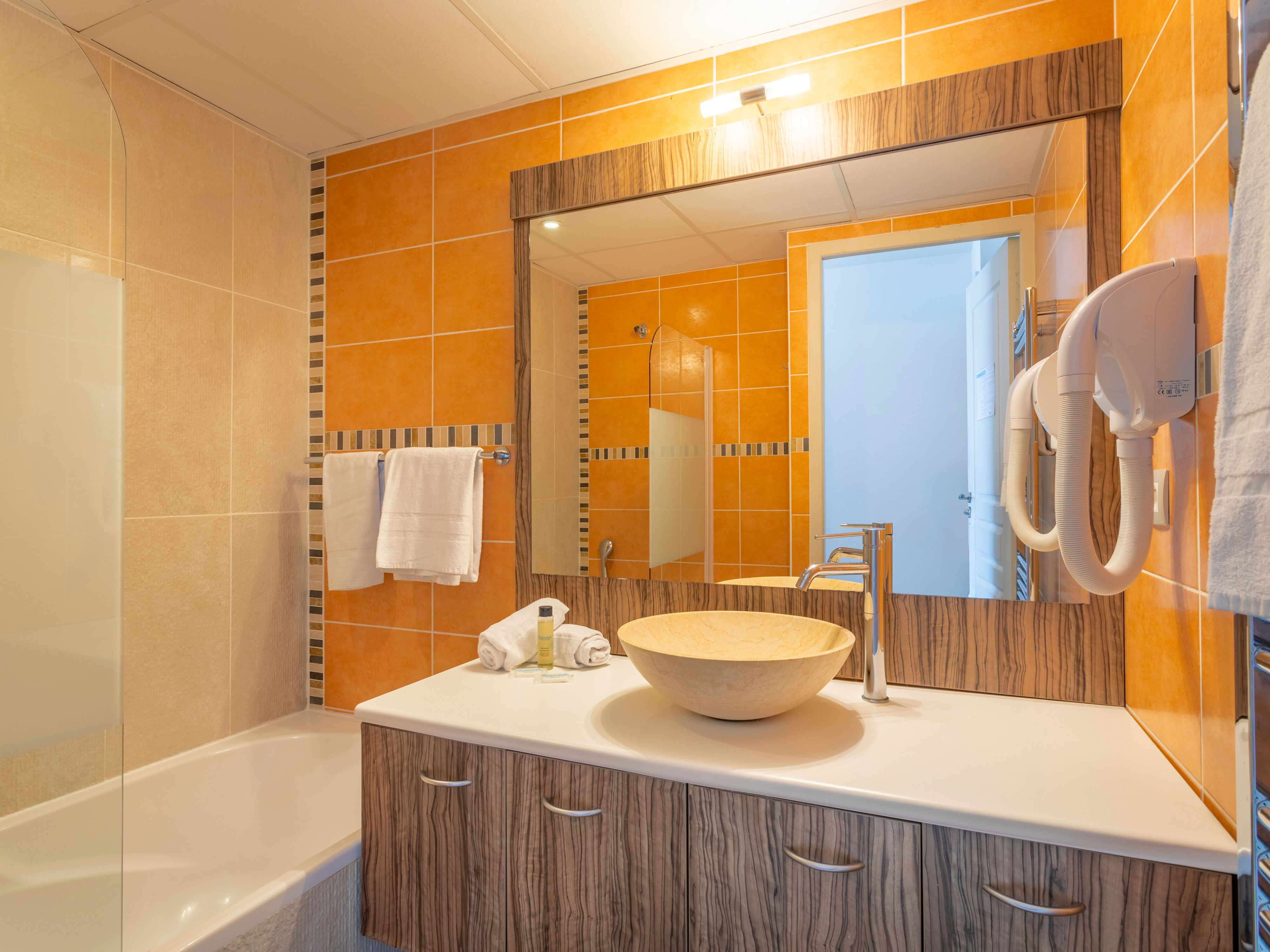 image En-suite bathroom with natural wood finishes, bathtub, and wall-mounted basin — fresh towels available on request