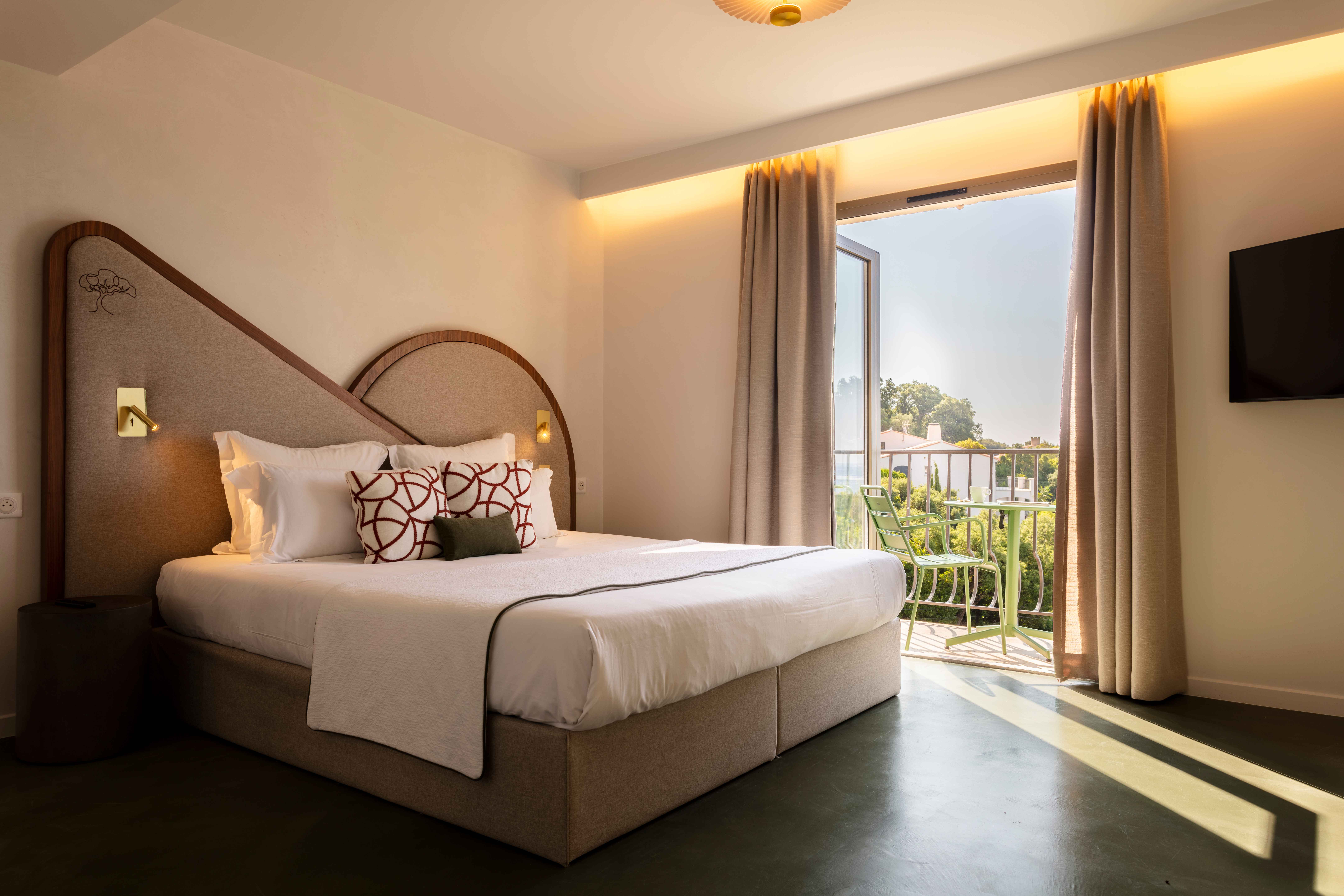 image White-linened bed with curved headboard — the south-facing balcony with green chairs is through the glass door