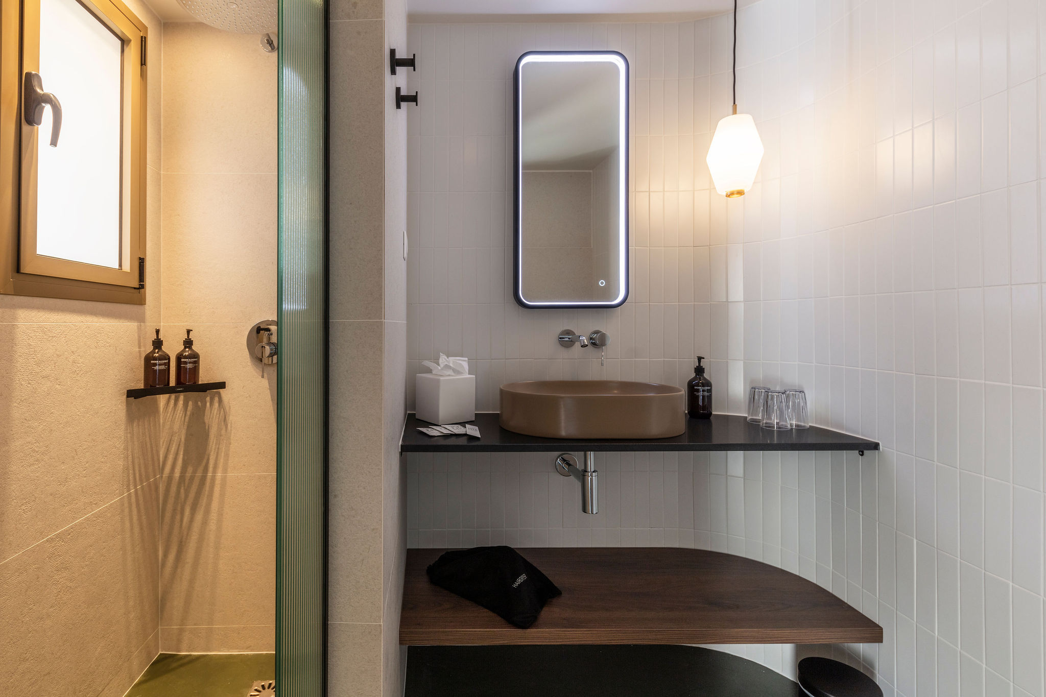 image White-tiled bathroom with a brown sink, backlit mirror, and a small window for natural light