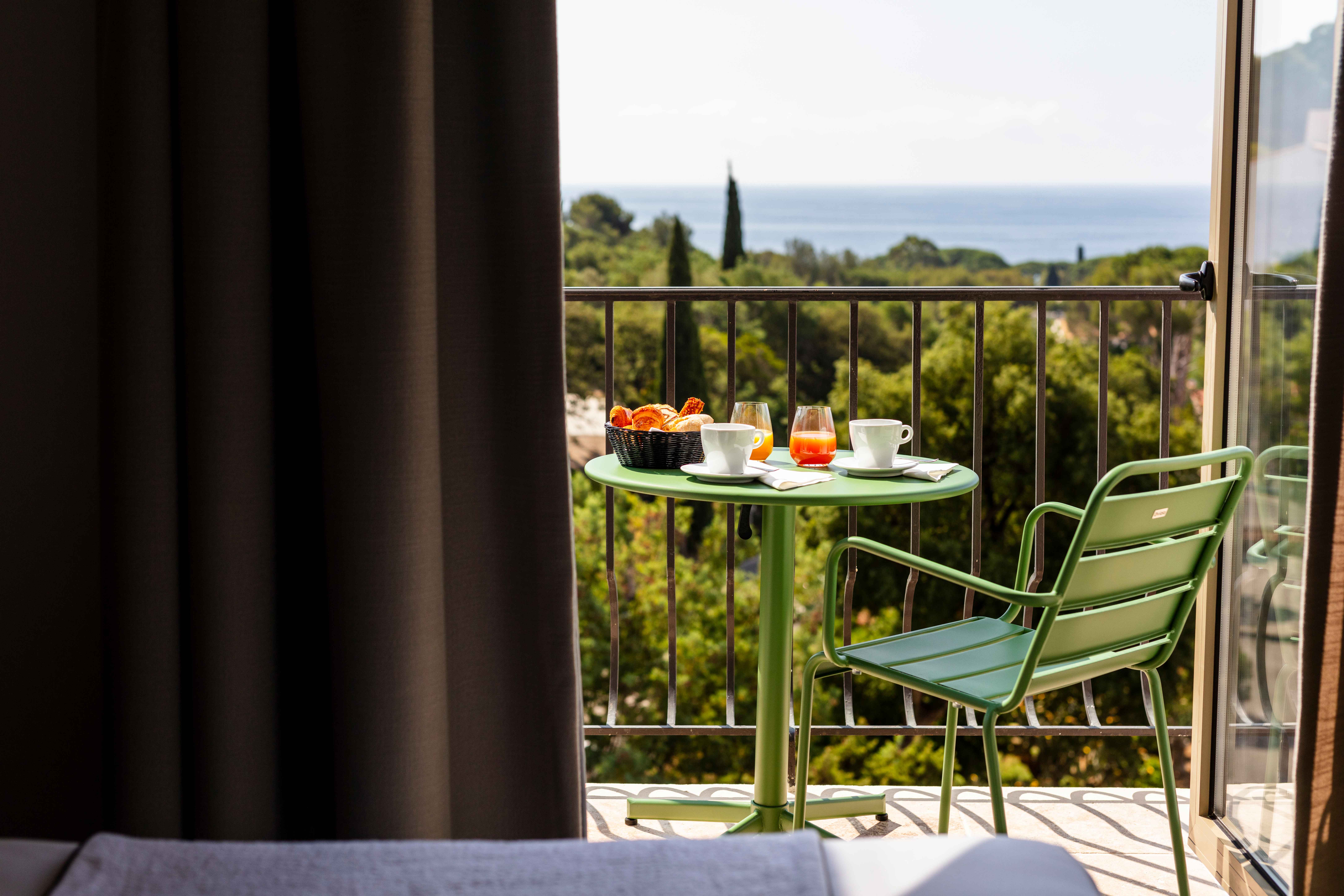 image Queen bed with patterned pillows — a green chair on the sea-view balcony through the open curtains