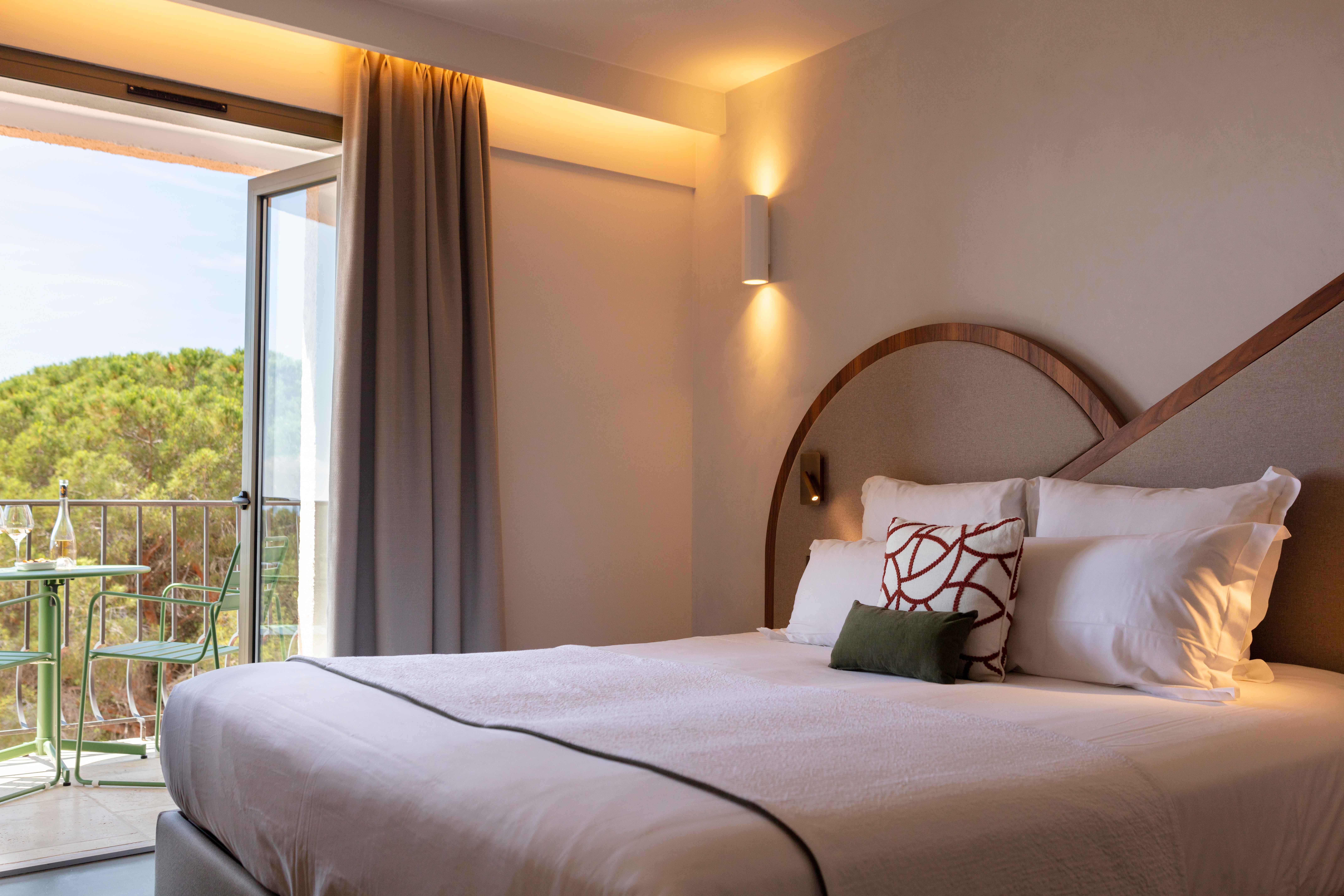 image King bed with wooden headboard and white linens — greenery from the park balcony visible behind