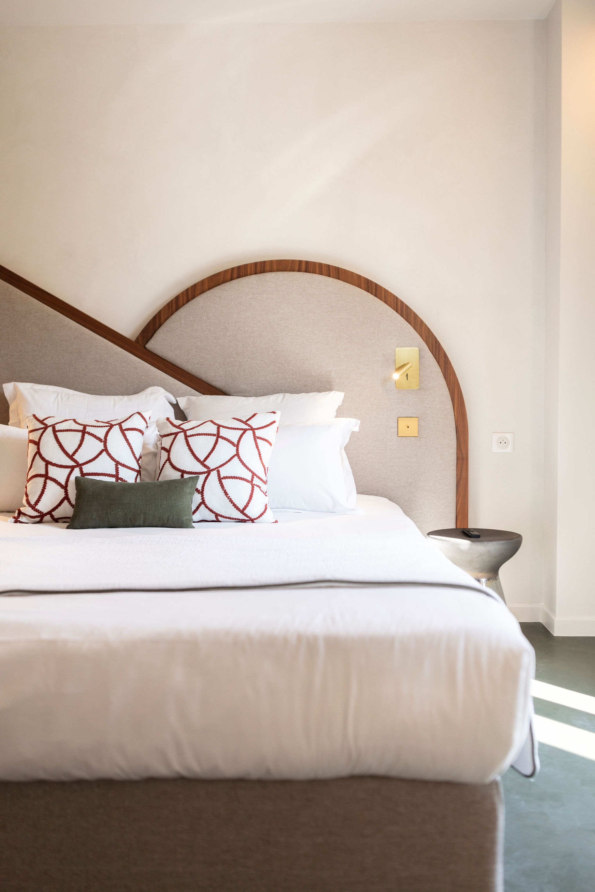 image Queen bed with a smooth wooden headboard, decorative pillows, and a metallic bedside stool