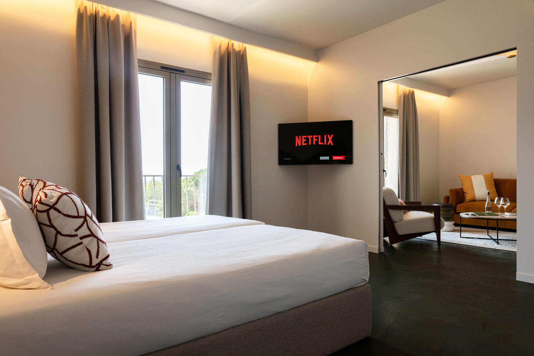 image Two single beds facing a wall-mounted TV, with grey curtains framing the outdoor view