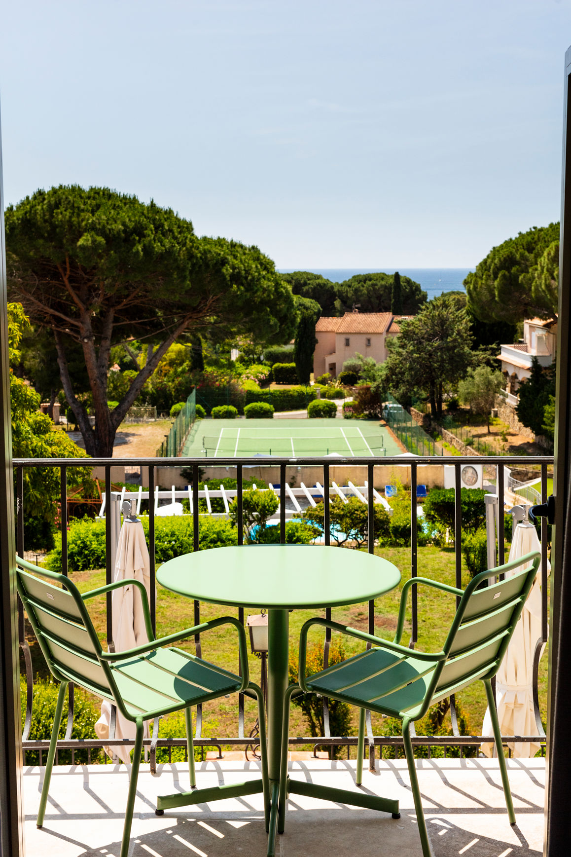 image Round green table and chairs on the balcony with the pool, tennis courts, and park spread below