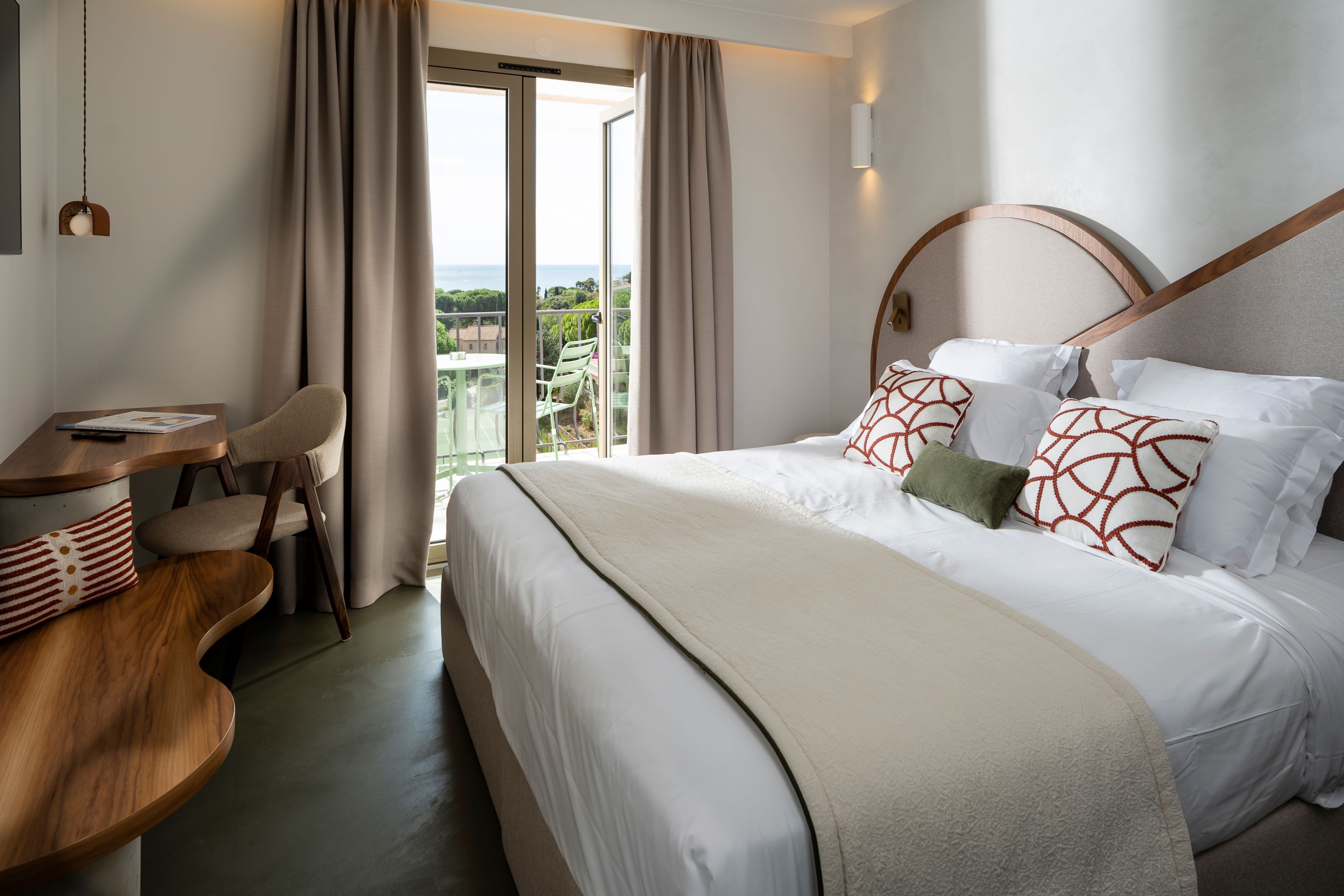 image Large bed with decorative pillows and a writing desk, with glass doors opening to the sea-view balcony