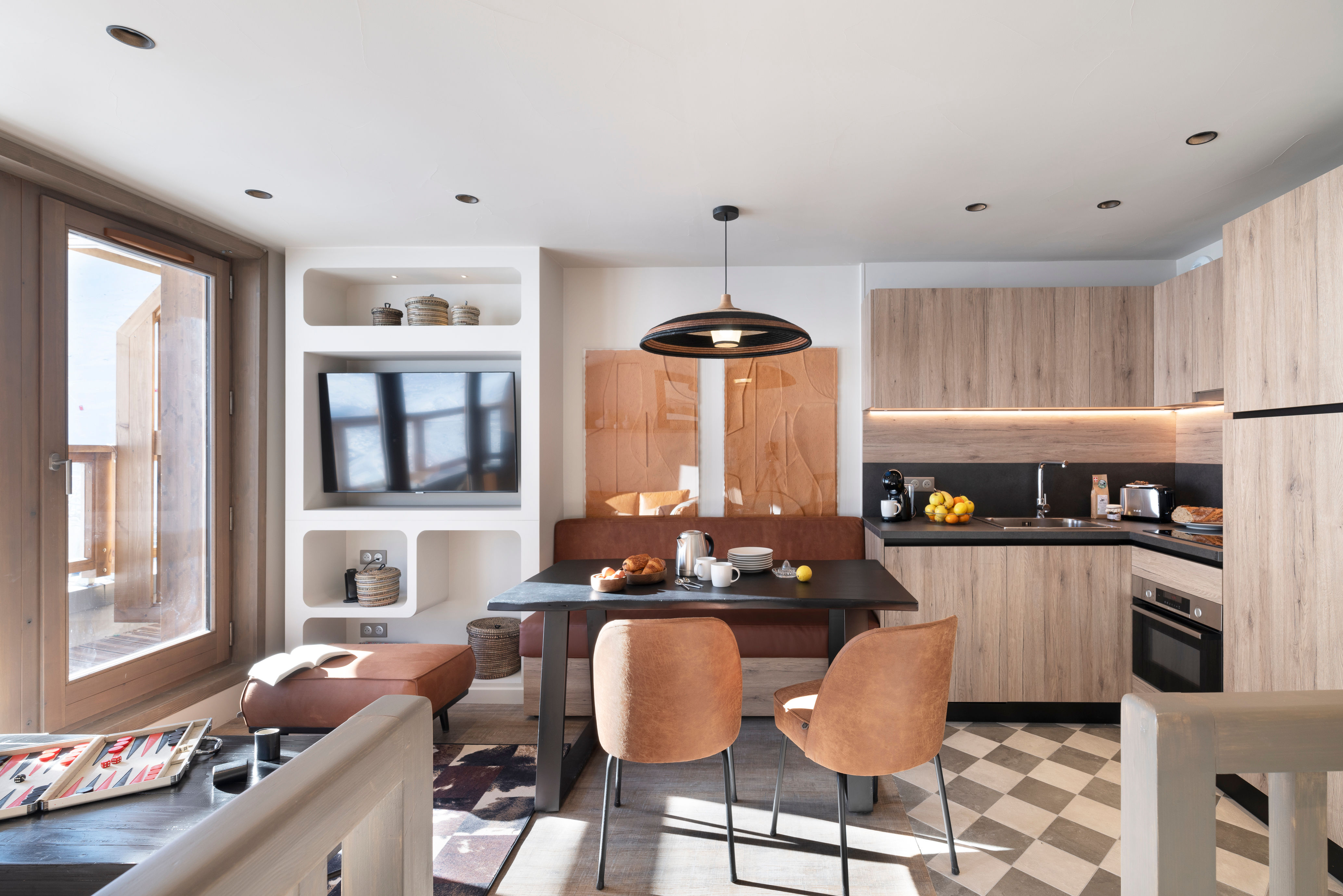 image Dining area with wall-mounted TV, black table, and warm wood chairs — bright natural light from the windows
