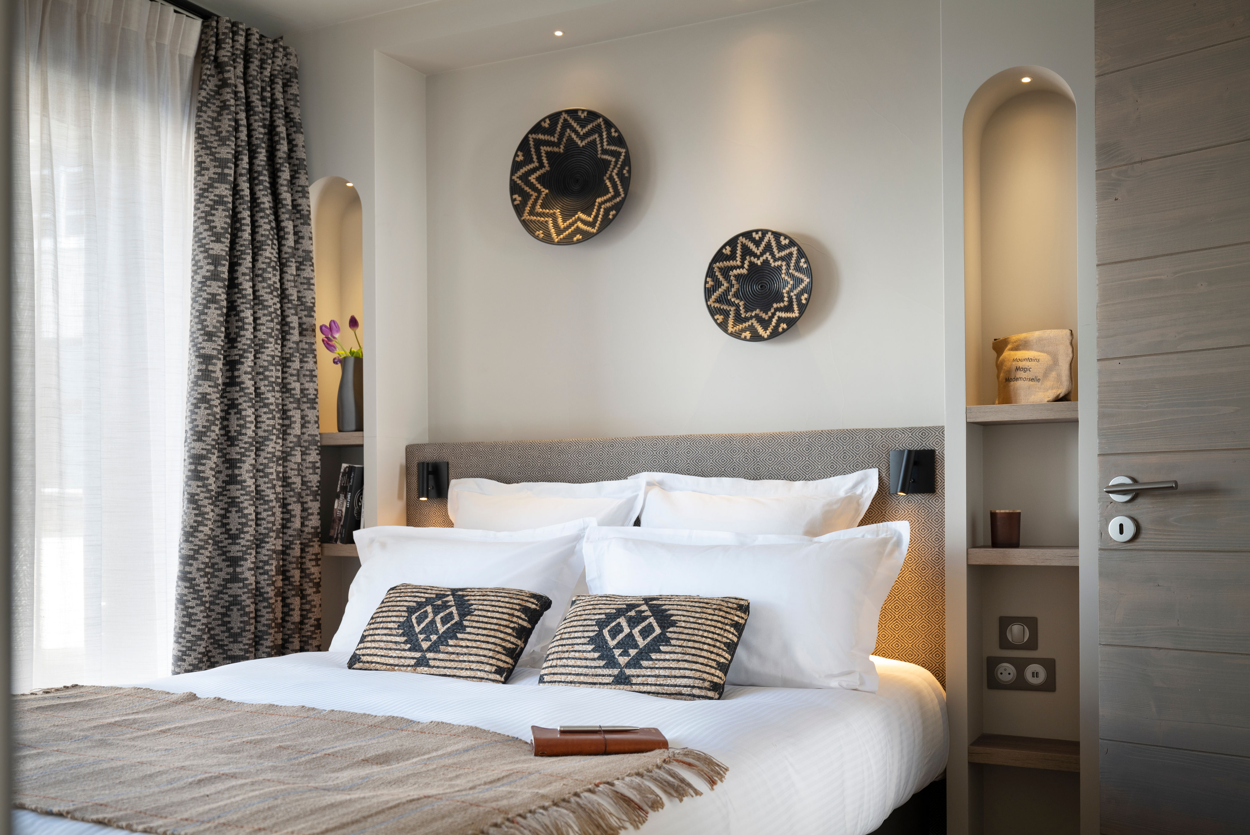 image Double bedroom with wall-mounted reading lamps, patterned curtains, and decorative wall plates in earthy tones