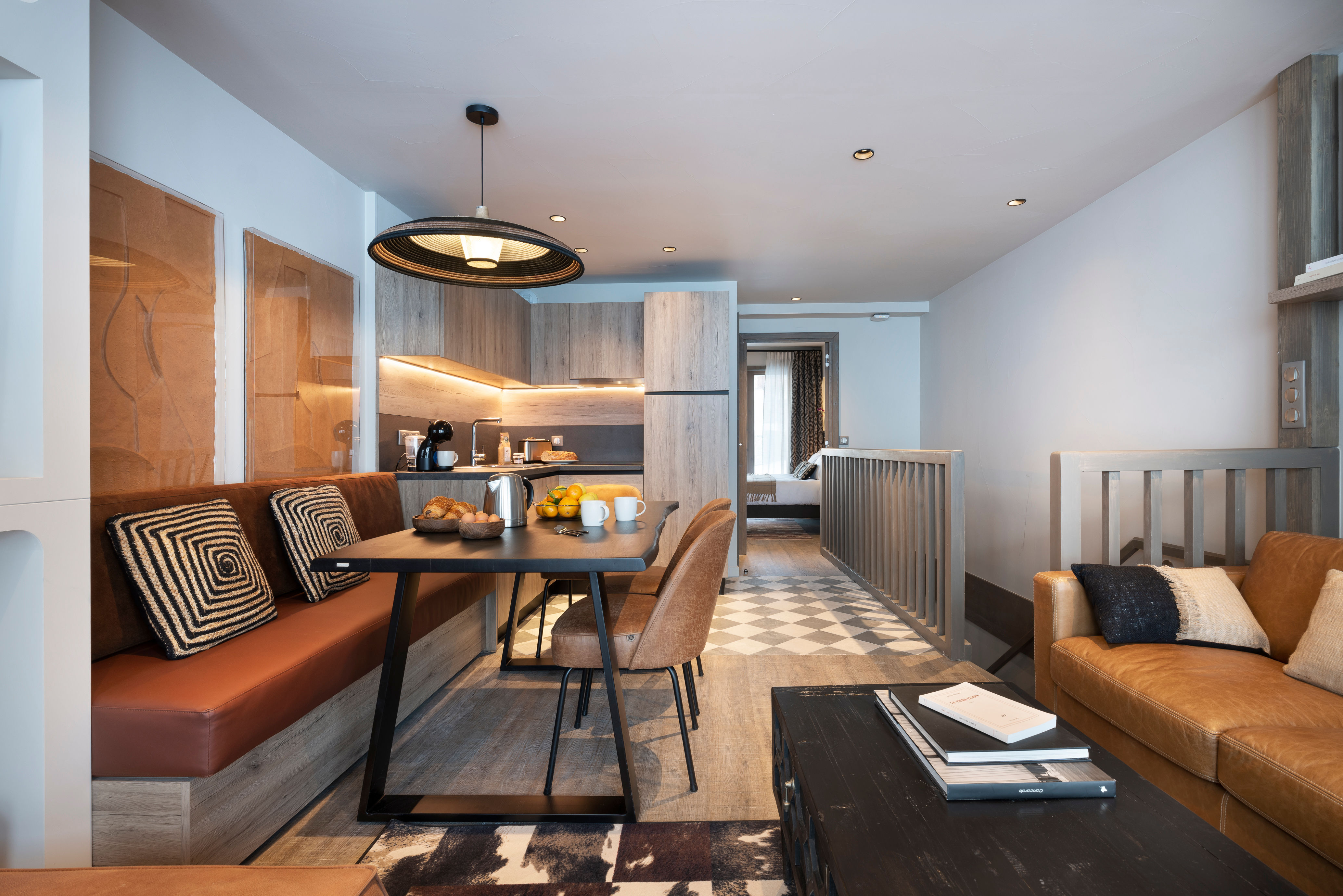 image Open-plan living and dining area with a pendant-lit table, kitchenette, and geometric-patterned soft furnishings