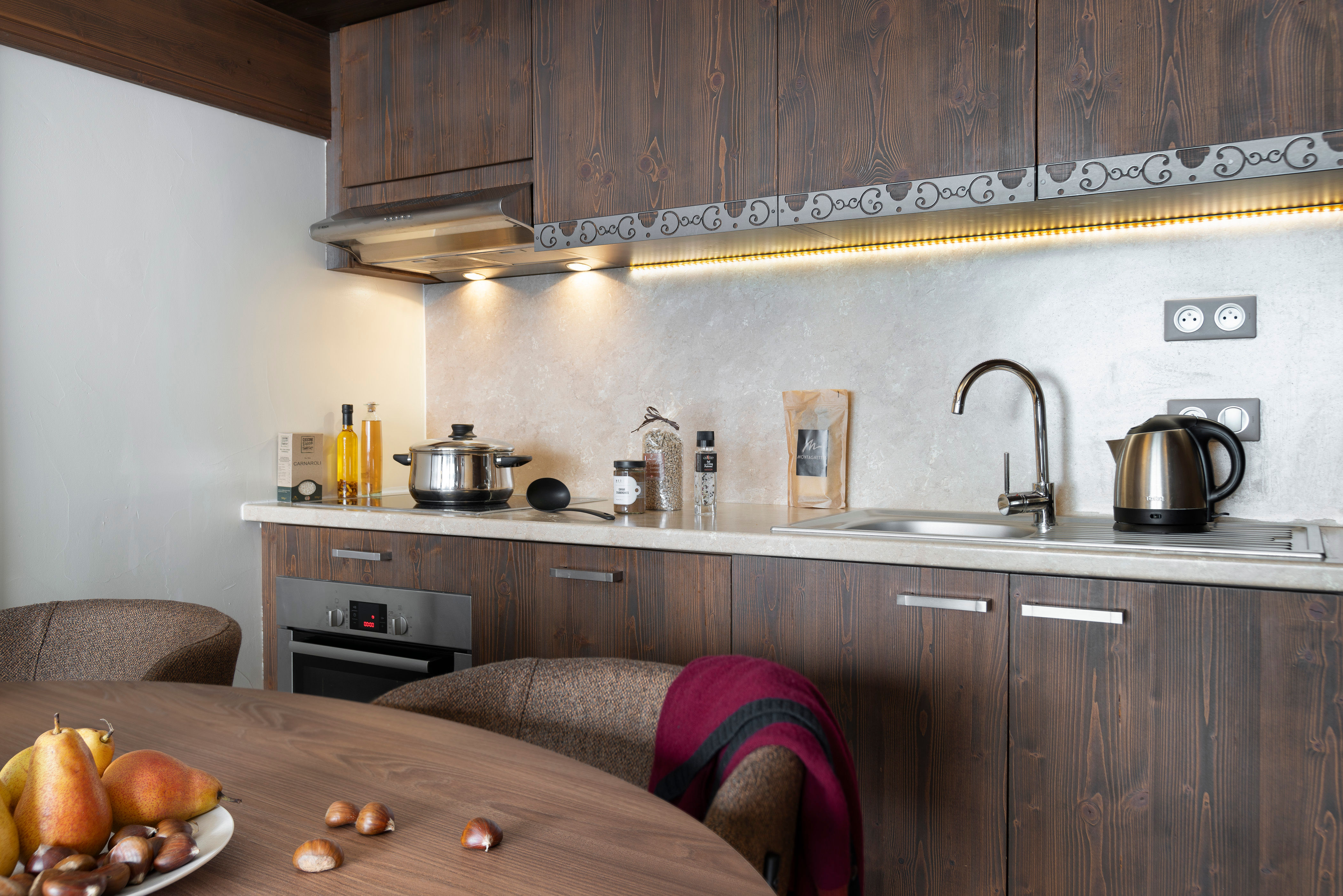 image Dark wood kitchen with under-cabinet lighting, ceramic hob, Nespresso machine, and kettle — all you need before heading out on a morning hike.