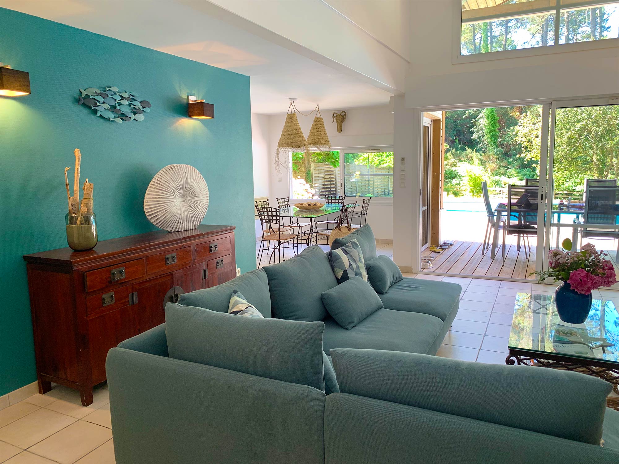 image The living room opens to the garden through wide windows — teal walls, a red sideboard, and plenty of natural light.
