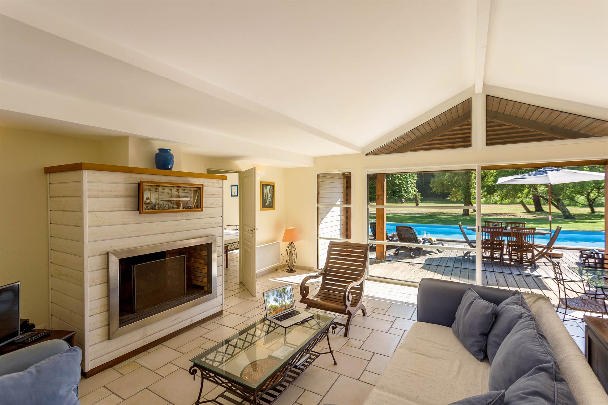 image Living room with a fireplace and glass coffee table — terrace doors open wide to the pool and garden beyond.
