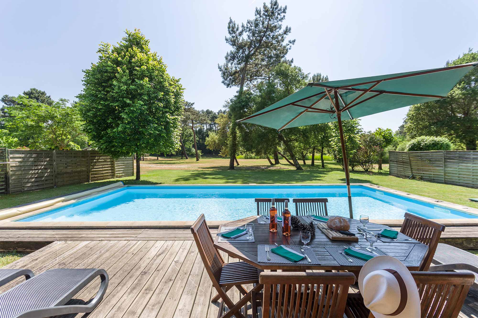 image Poolside dining under a parasol on the timber deck — the garden backs onto the pines with the lake close by.
