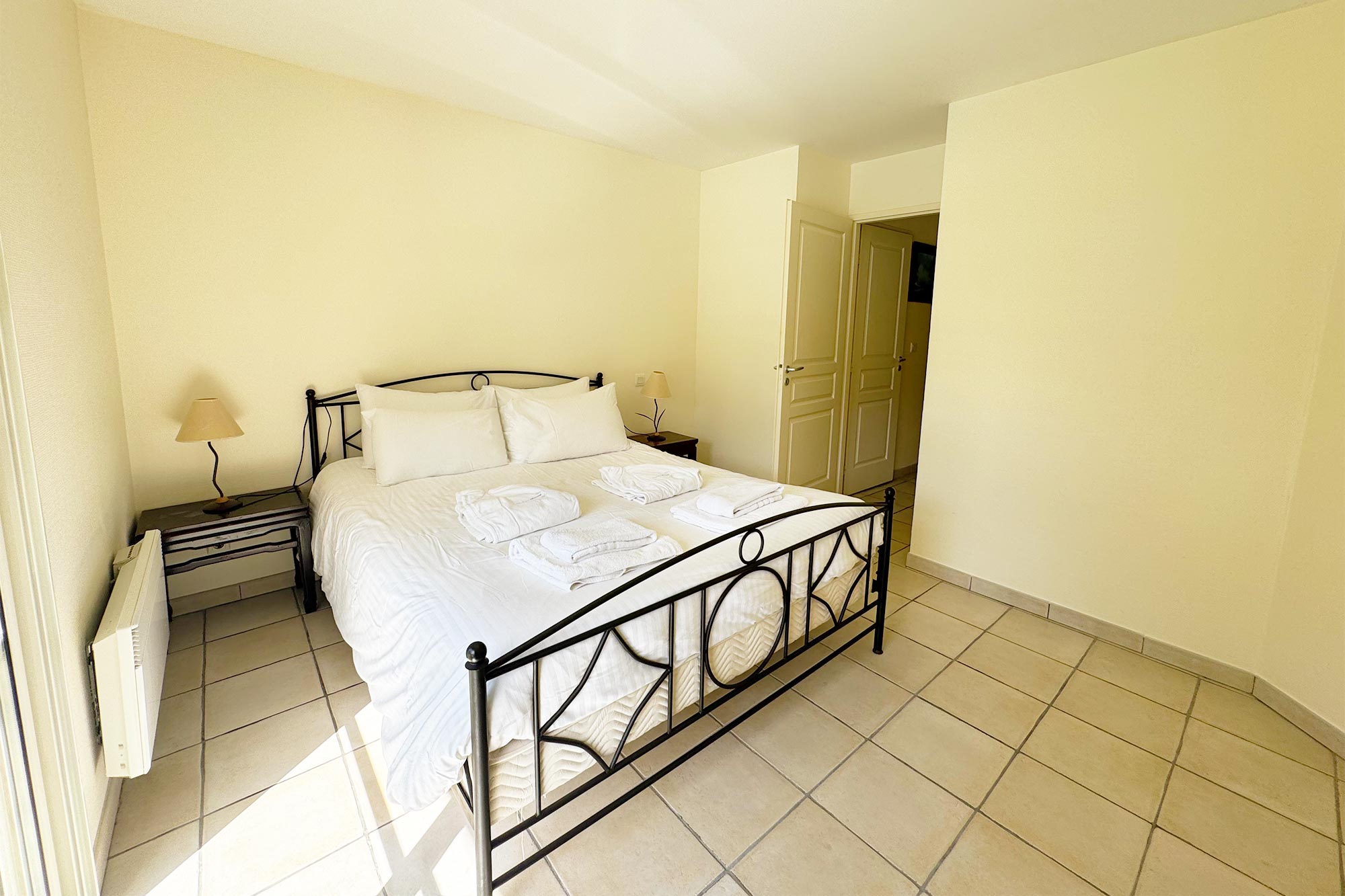 image Iron-frame double bed with white linen in a quiet, garden-facing bedroom with warm-toned walls.