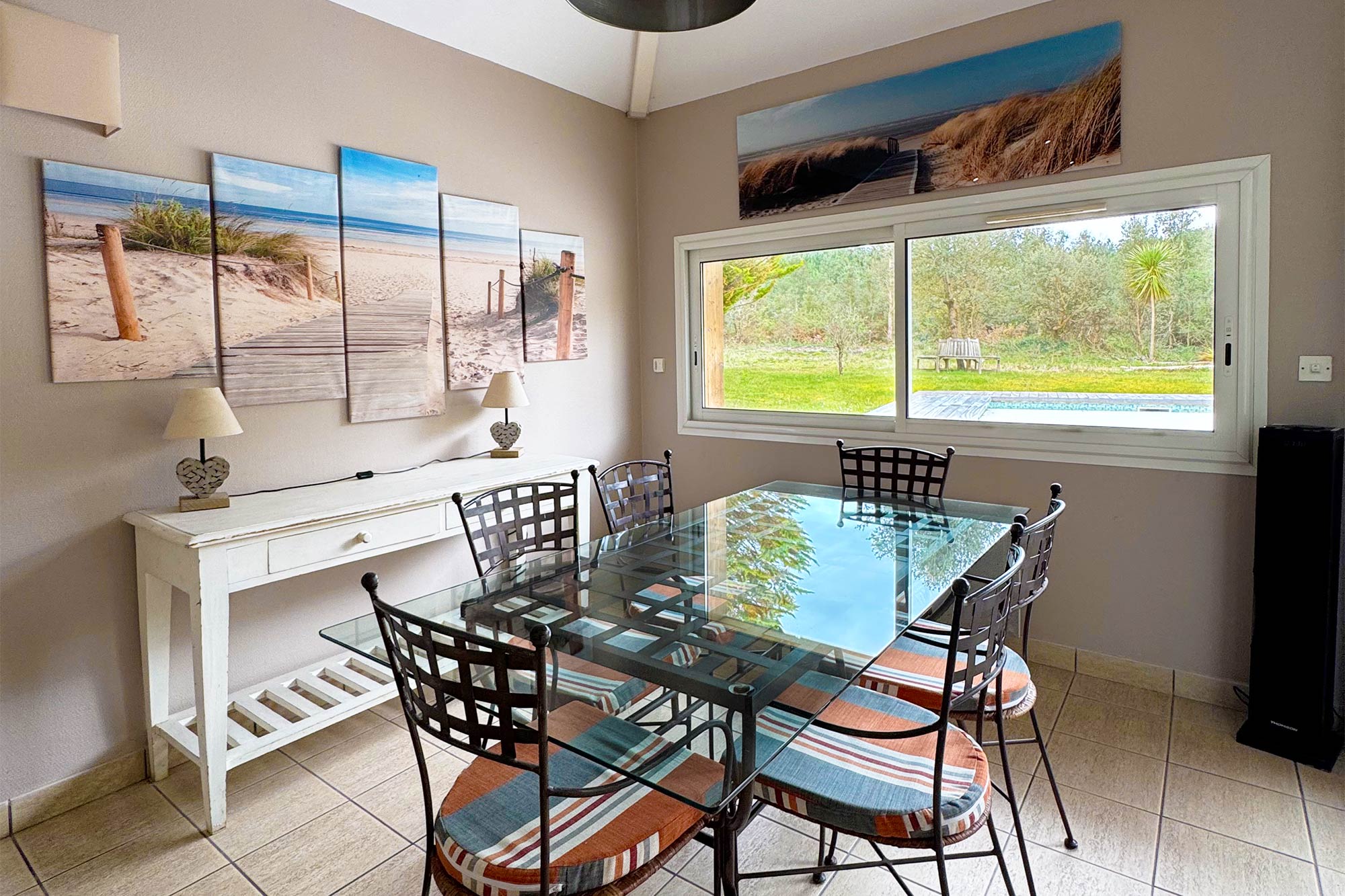 image Dining area with glass table and chairs, large window overlooking greenery, coastal canvas above:
Gather around the dining table with garden views framed in the window — the forest is right outside your door.
