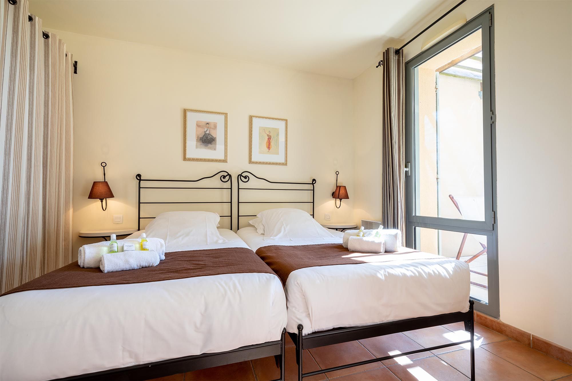 image A neatly presented twin bedroom with classic wrought-iron beds and warm Provençal tones.