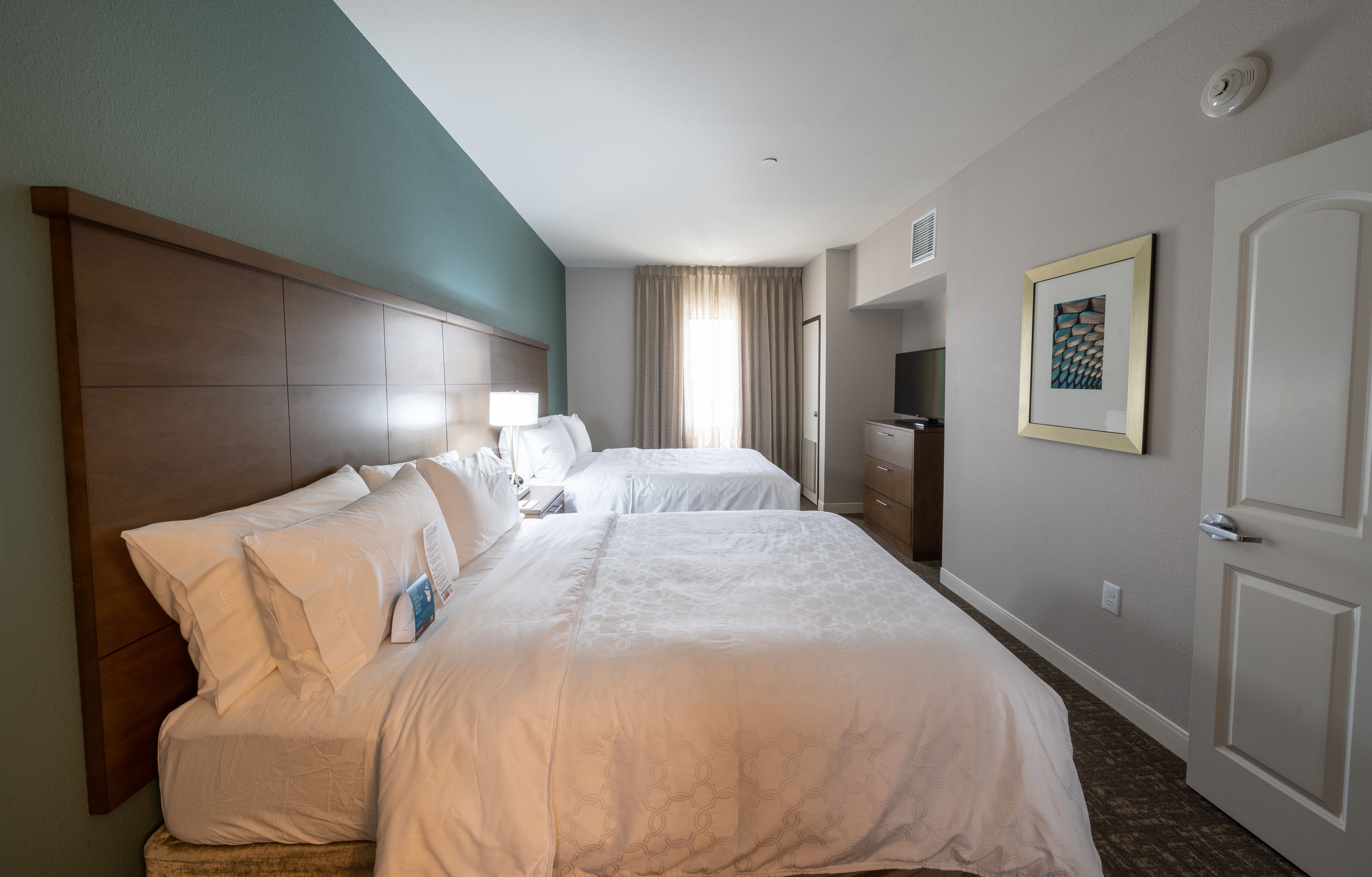 image Relax in a spacious bedroom with two plush queen beds and soft lighting for a cozy ambiance.