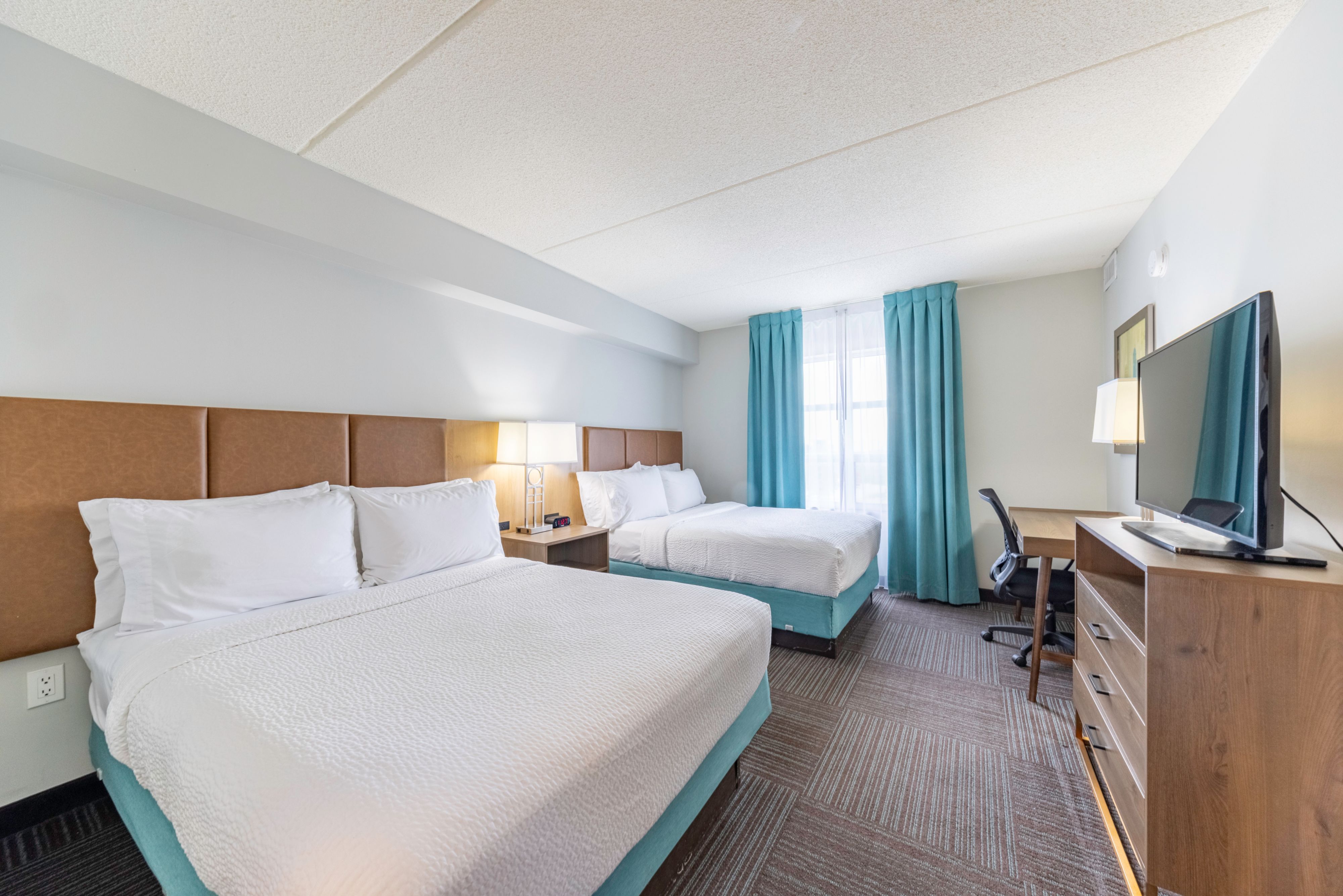 image Comfortable bedroom with two beds, desk, and wall-mounted television.