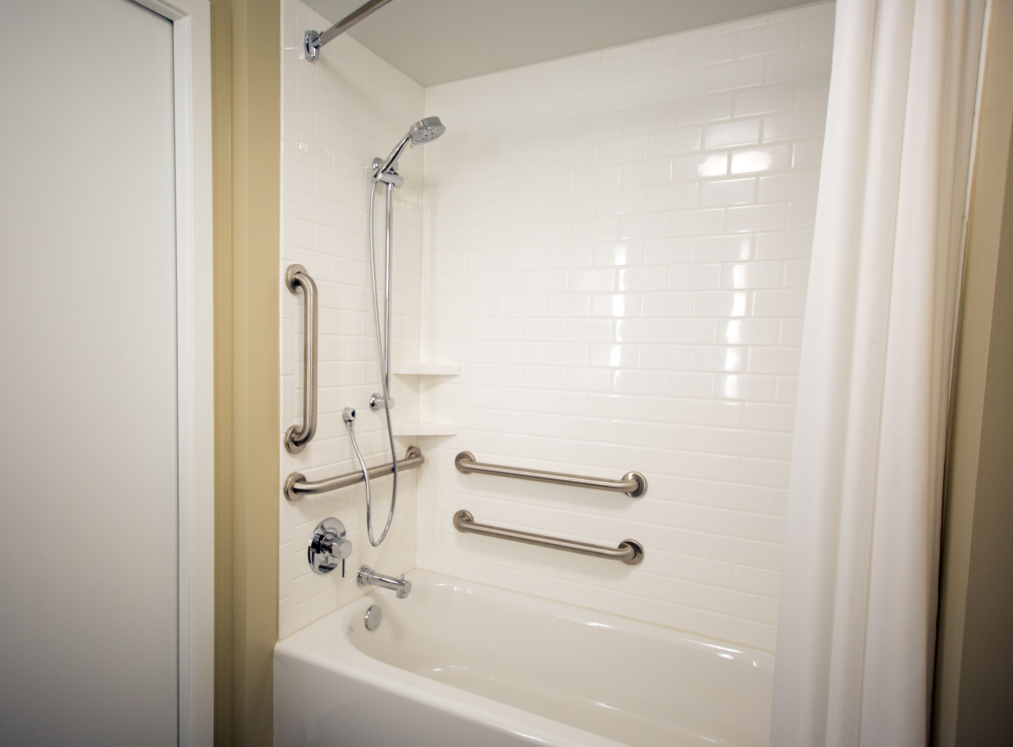 image Accessible bathroom with tub, shower, white tiles, and grab bars.