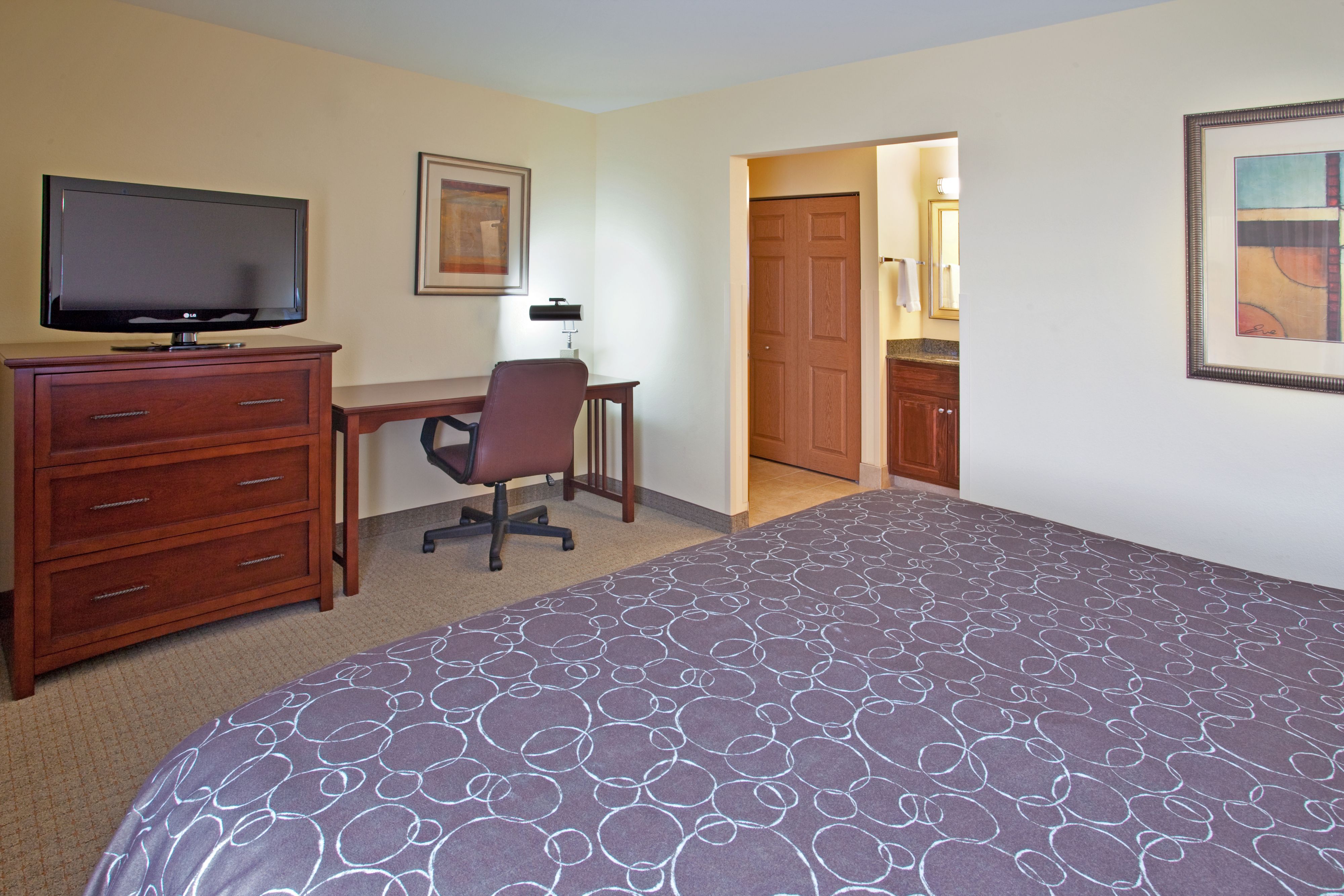 image Cozy bedroom with large bed, dresser, desk, and flat-screen TV.