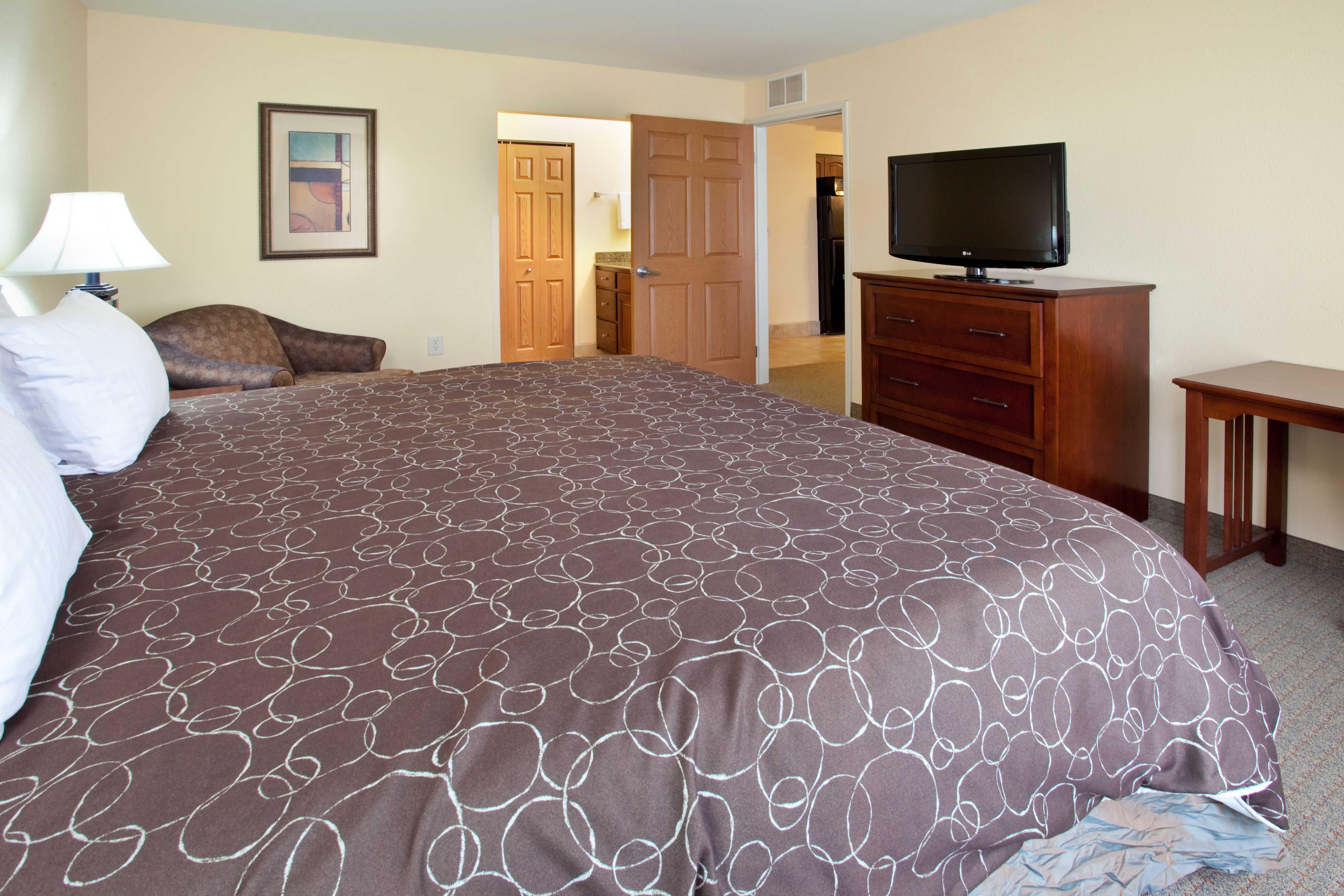 image Bedroom with spacious bed, dresser, seating area, and flat-screen TV.