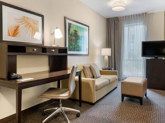image Living area with sofa, ottoman, work desk, rolling chair, and flat-screen TV