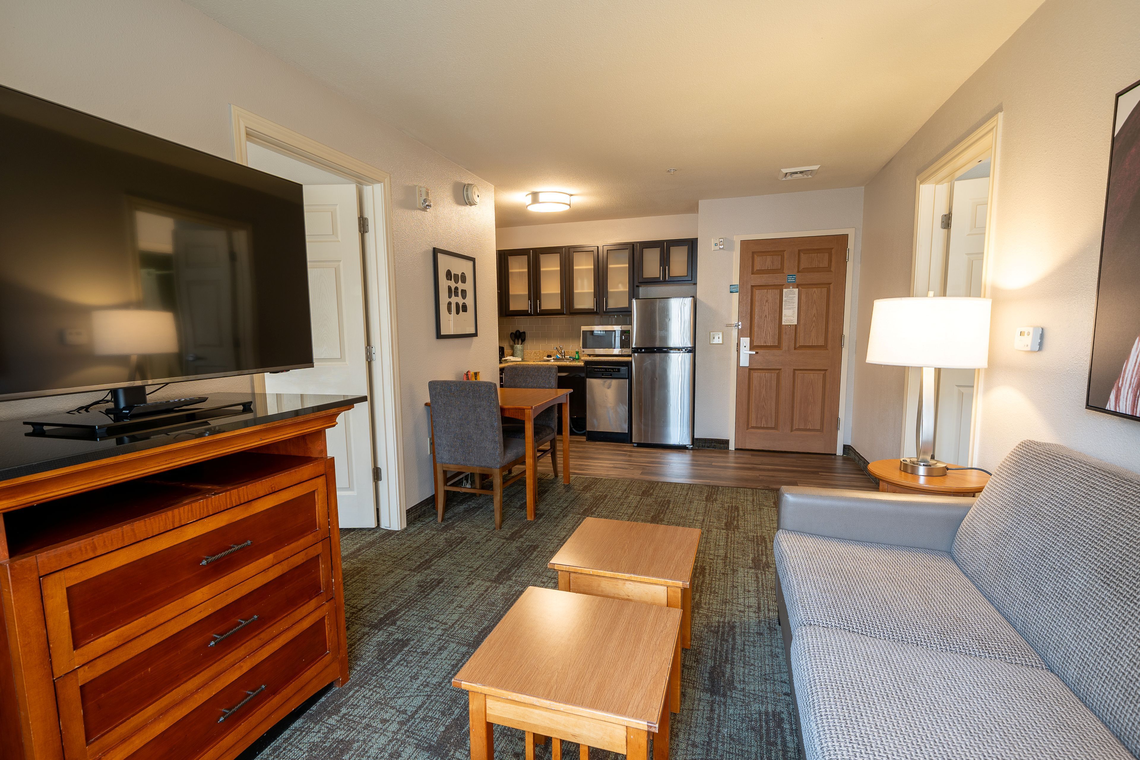 image Living area with a flat-screen TV, sofa, and a dining table beside the kitchen.