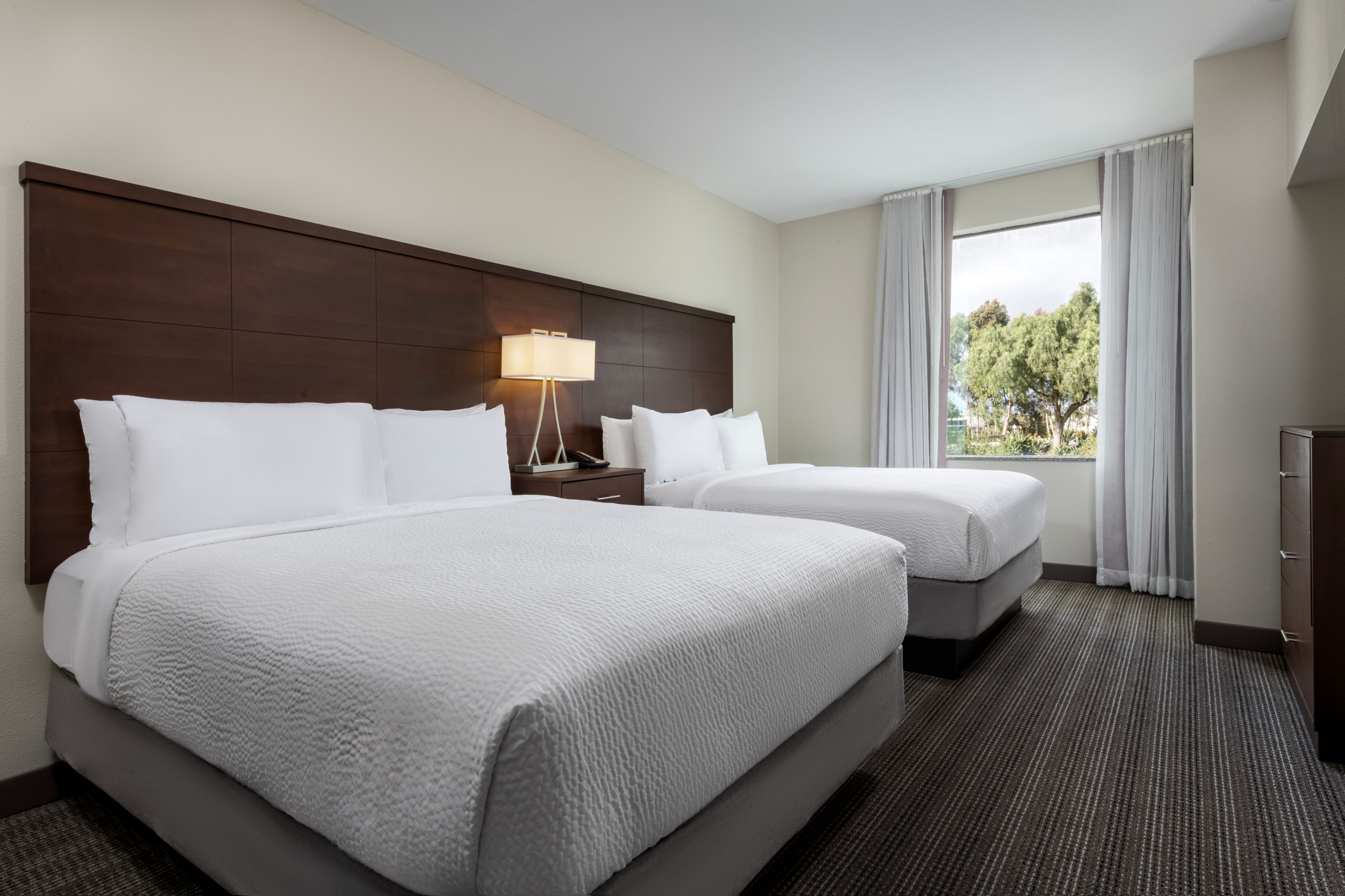 image Two neatly made beds with white linens, lamps, and window view.